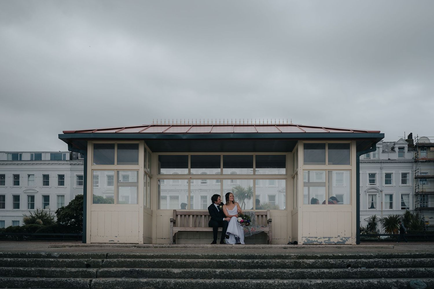 Wedding couple in a vintage seaside shelter against moody grey skies.