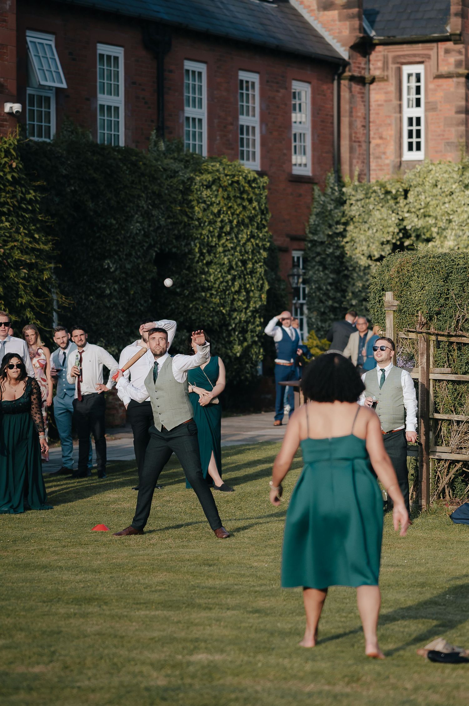 Wedding guests enjoy outdoor lawn games near a brick building.