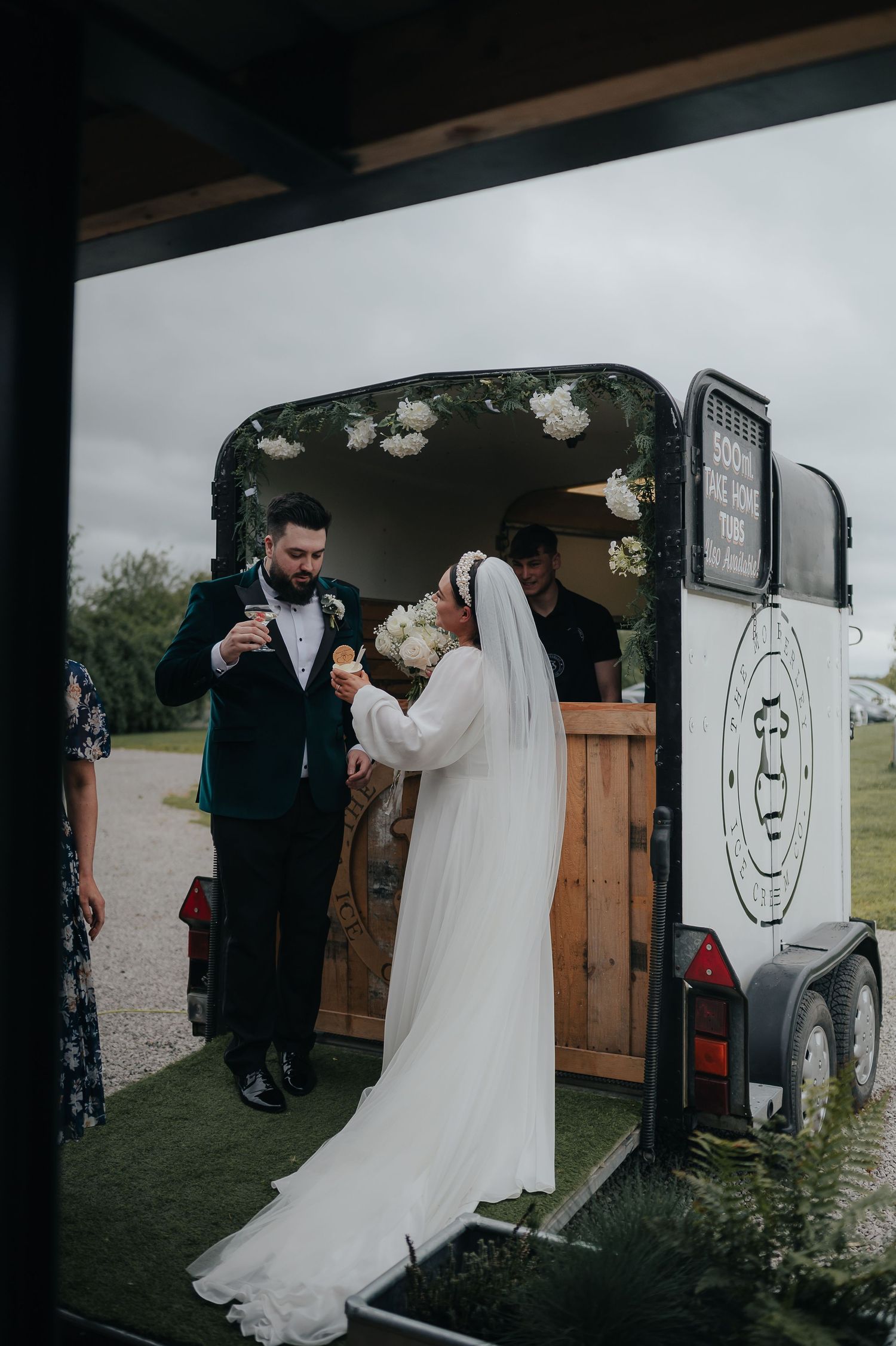 Couple enjoys refreshments at rustic mobile bar trailer during outdoor wedding reception.