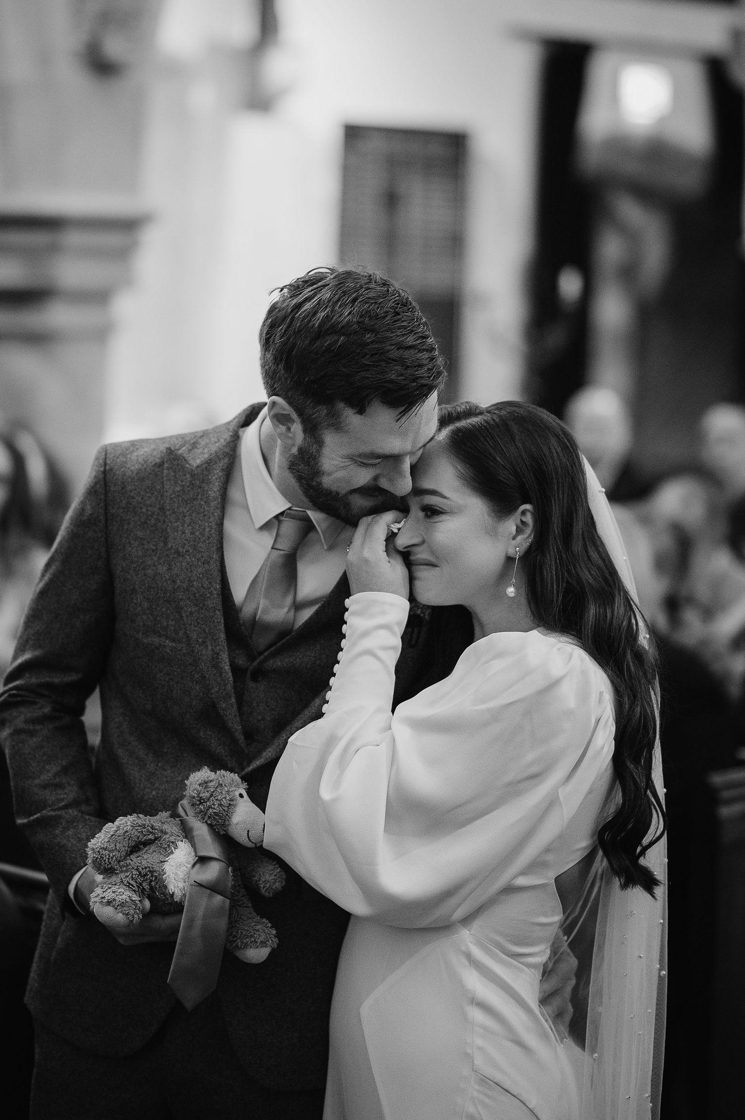A tender black and white moment between newlyweds with a small teddy bear during their wedding celebration.