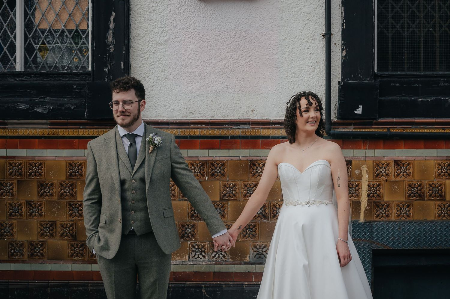 A romantic moment shared against a decorative tiled wall in urban setting.