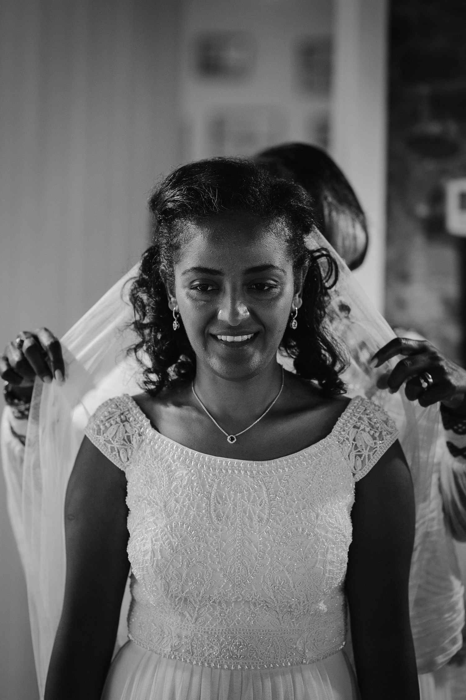 Black and white photo of a bride smiling in a lace wedding dress with a delicate veil.