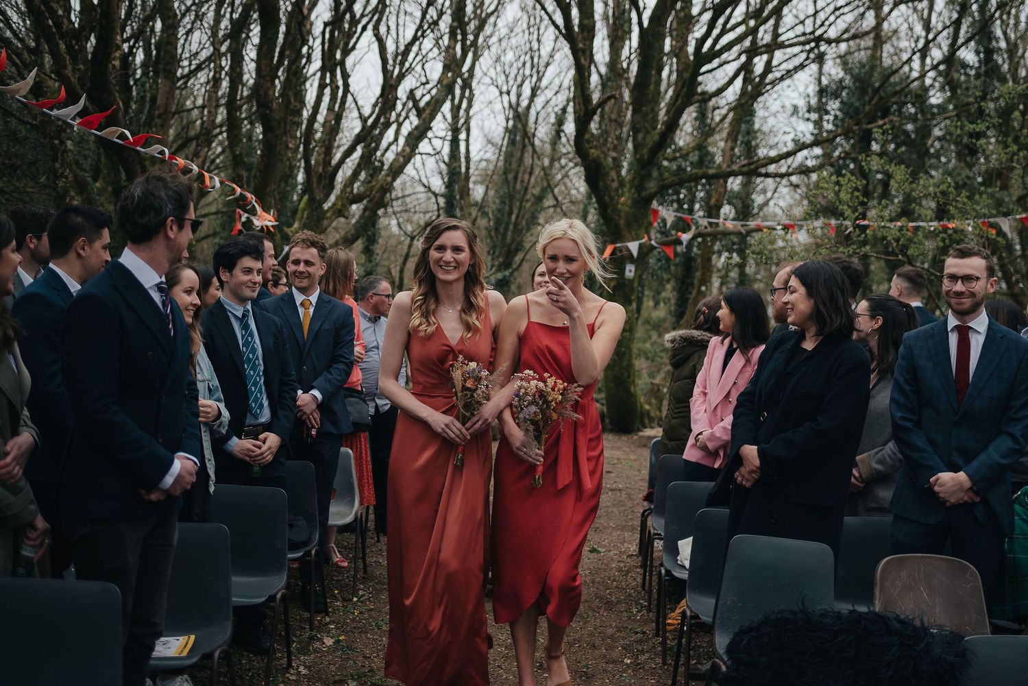 Outdoor wedding ceremony with attendees gathered along wooded path.