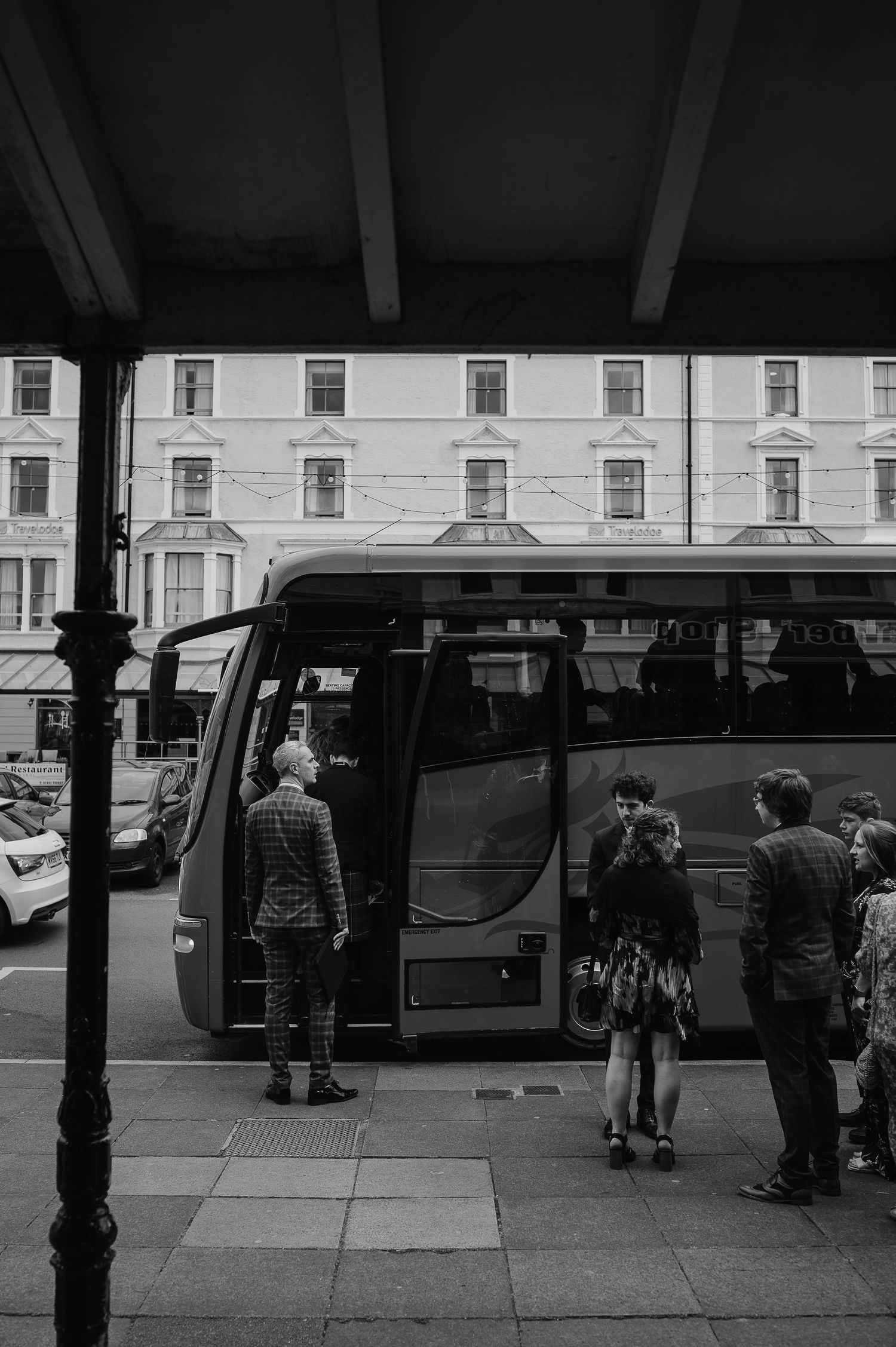People boarding a large tour bus parked outside a row of Victorian buildings.
