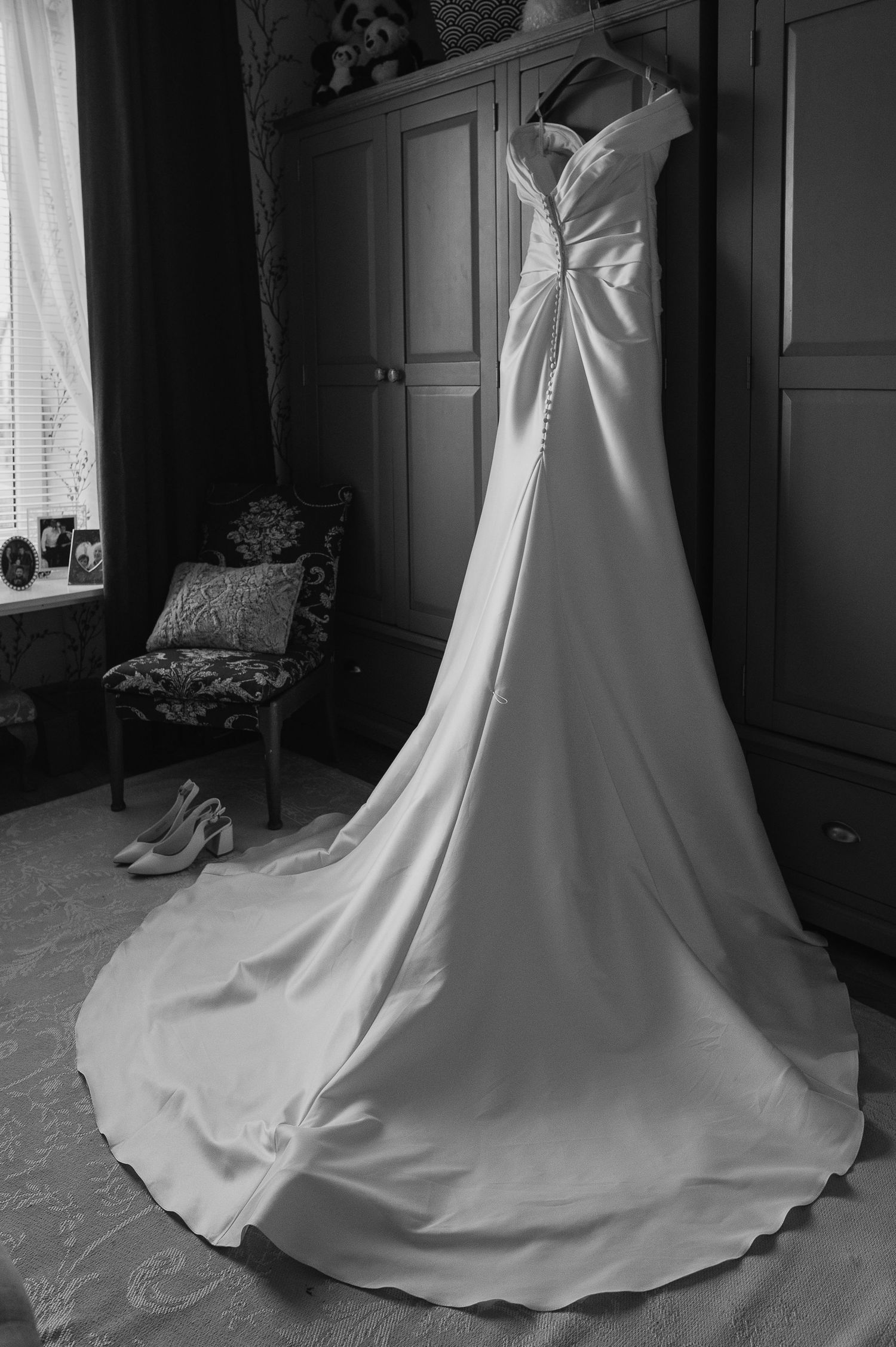 Elegant white wedding dress with long train hanging in a vintage room with antique furniture.