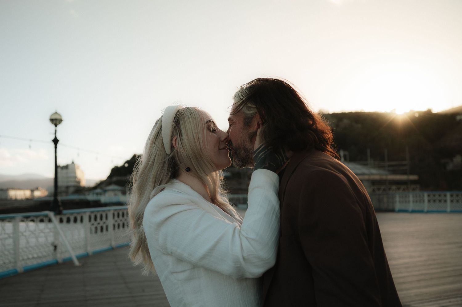 A romantic couple shares intimate moments on a pier at sunset with dramatic lighting.