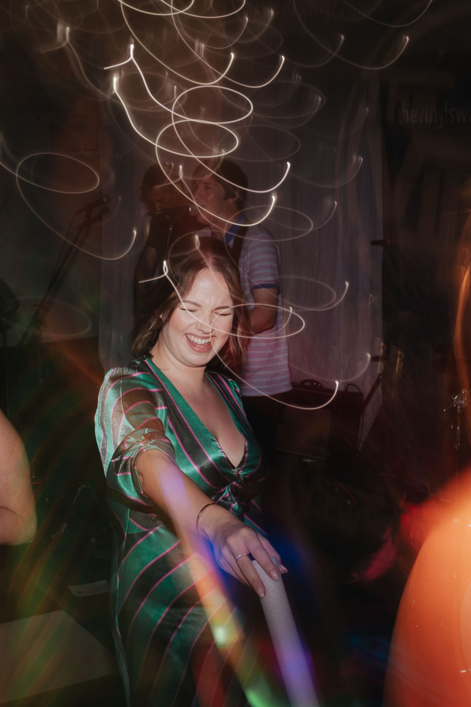 A woman in a green dress dances under swirling light patterns at a nightclub.