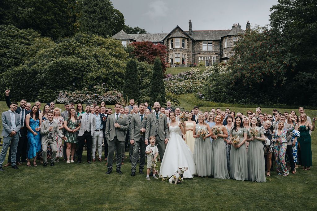 Large wedding party gathered on a manor house lawn for a group photograph.