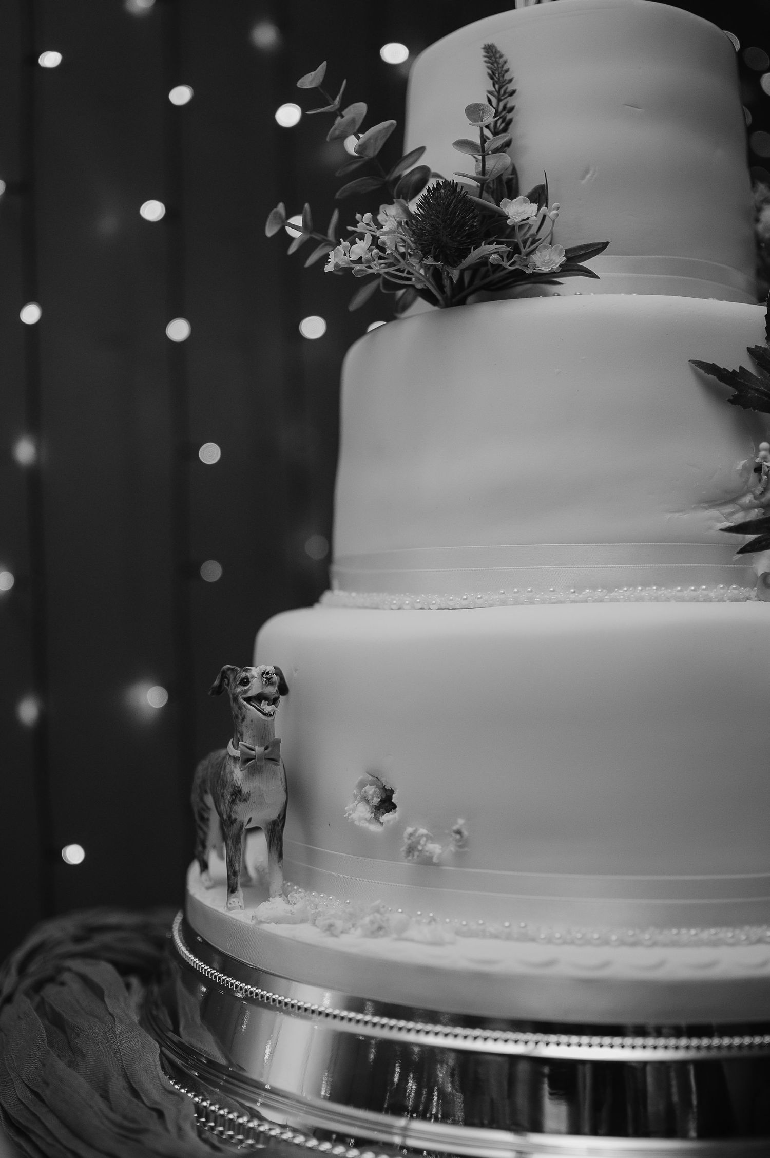 Elegant white wedding cake with floral decorations and small animal figurines against sparkly background.