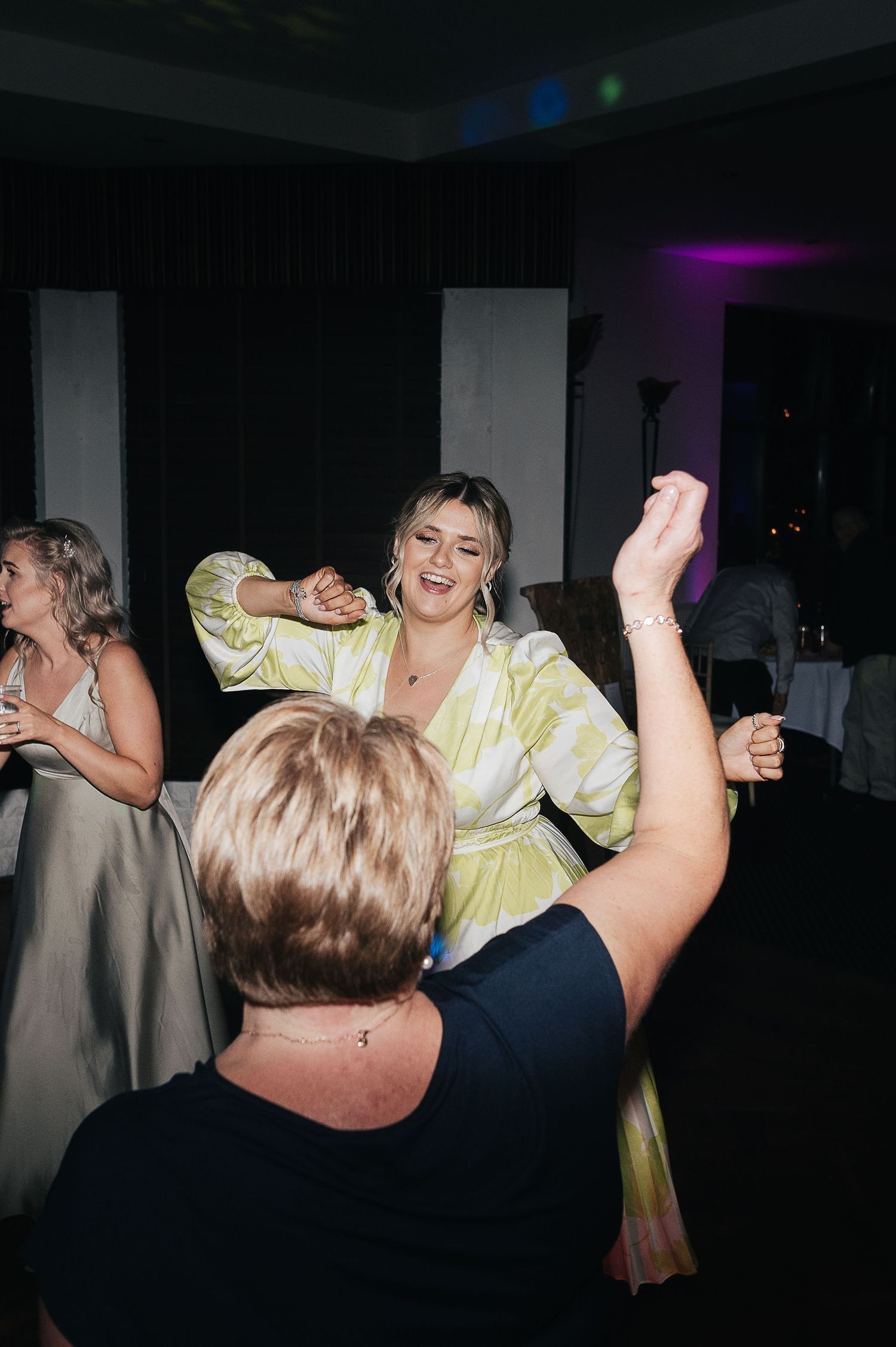 Wedding guests dancing enthusiastically at a dimly lit reception party.