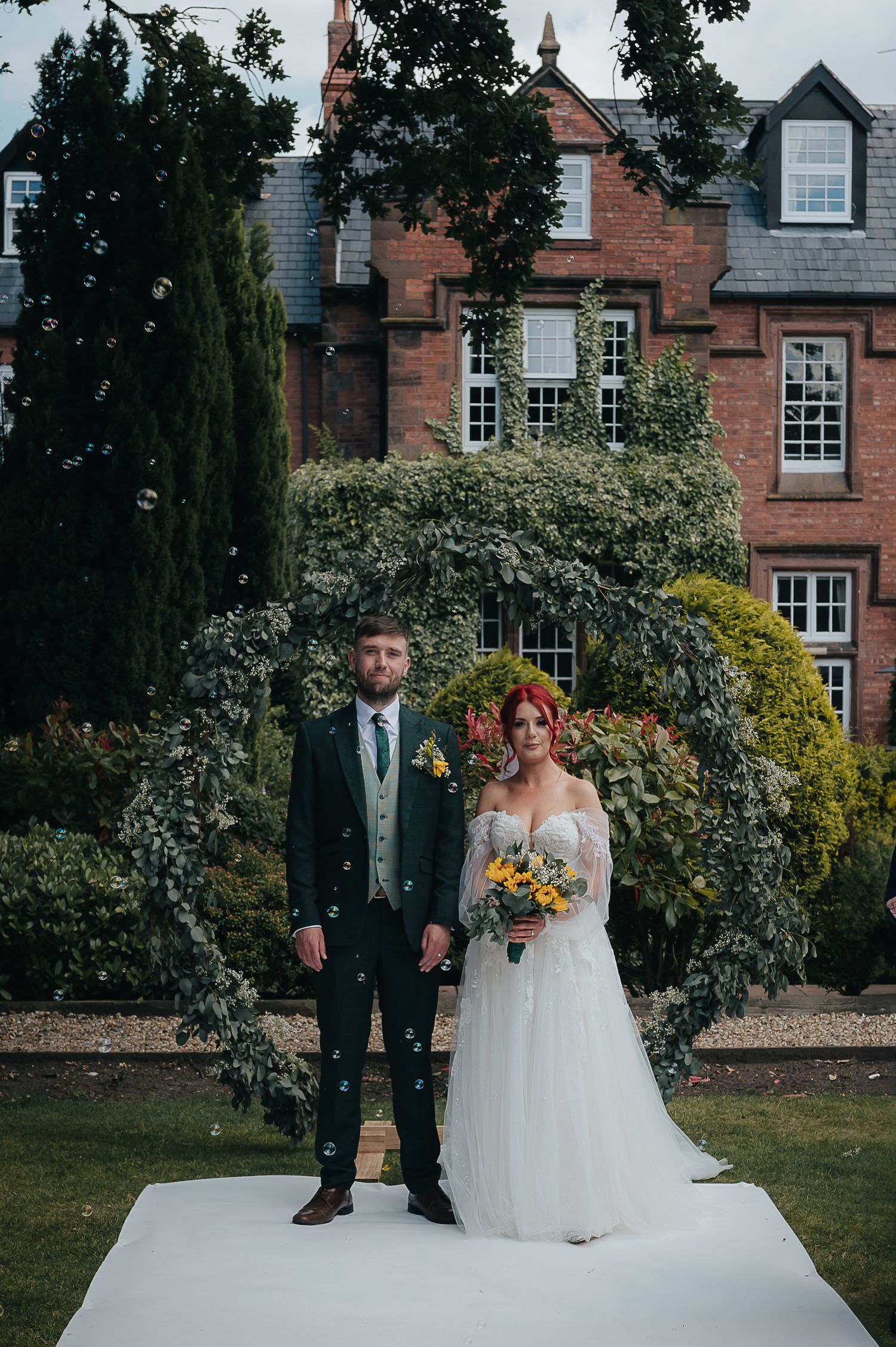 A wedding portrait in front of a beautiful brick mansion with landscaped gardens.