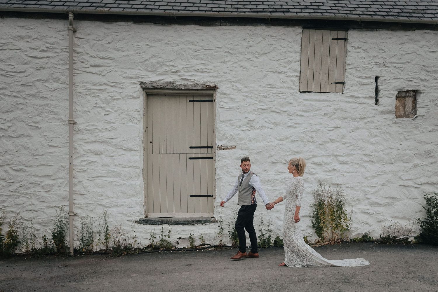A couple walks along a whitewashed wall with a rustic wooden door.