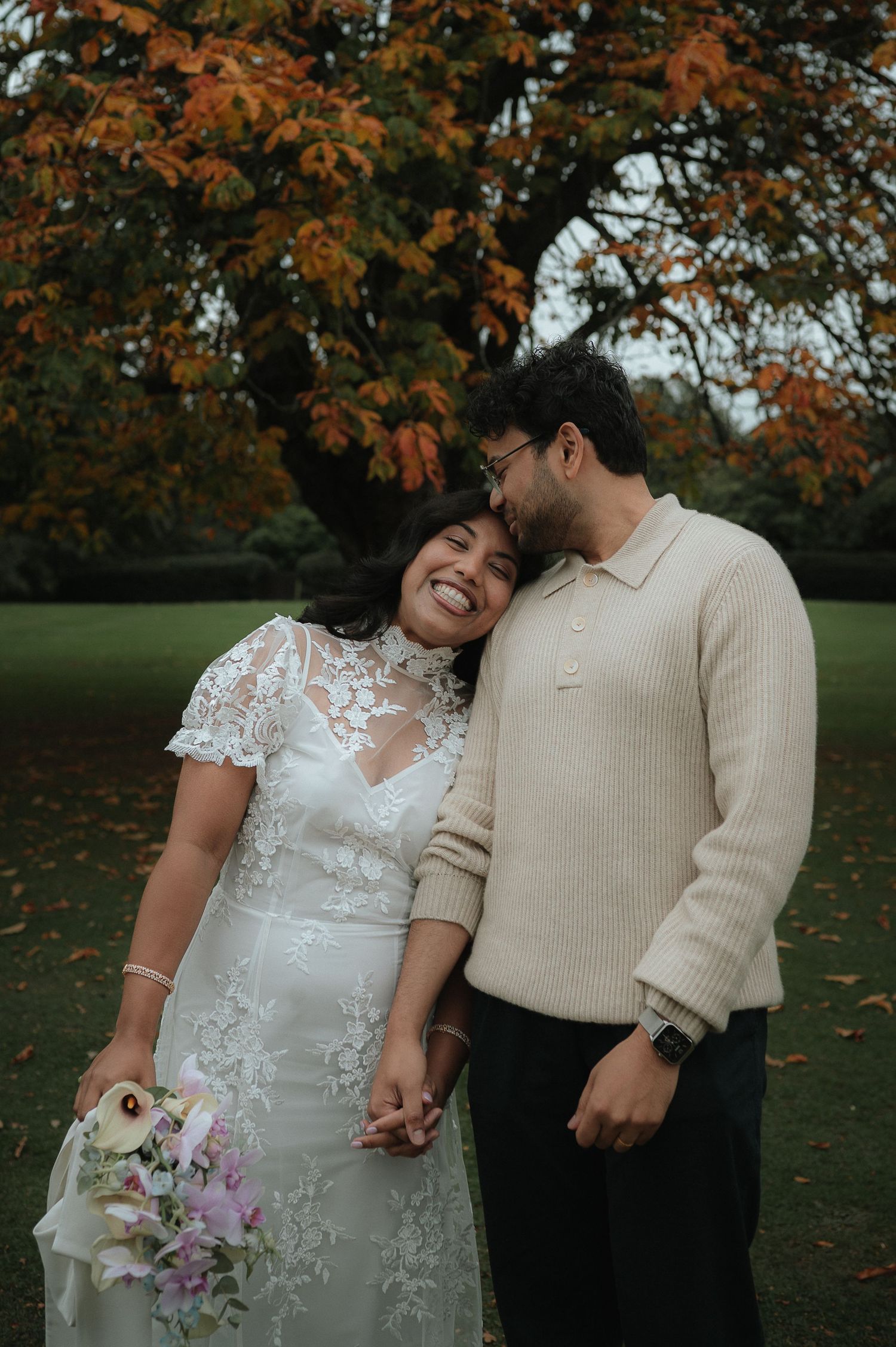 A couple in wedding attire shares intimate moments in an autumn setting with orange-leaved trees in the background.