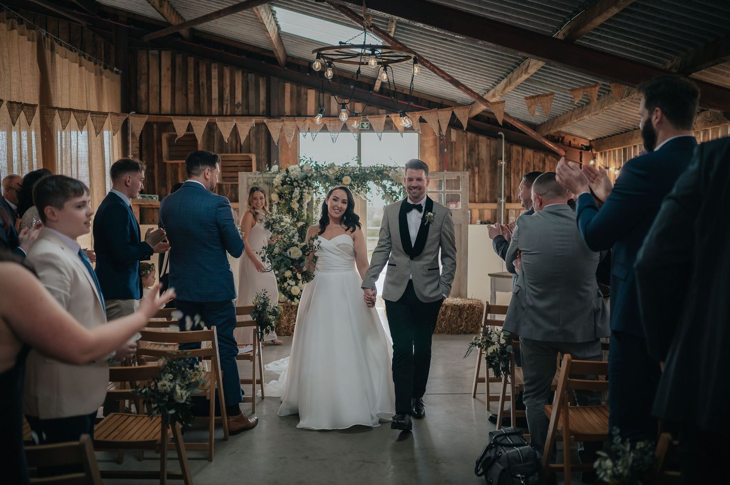 Newlyweds walk down the aisle in a rustic barn venue after their wedding ceremony.