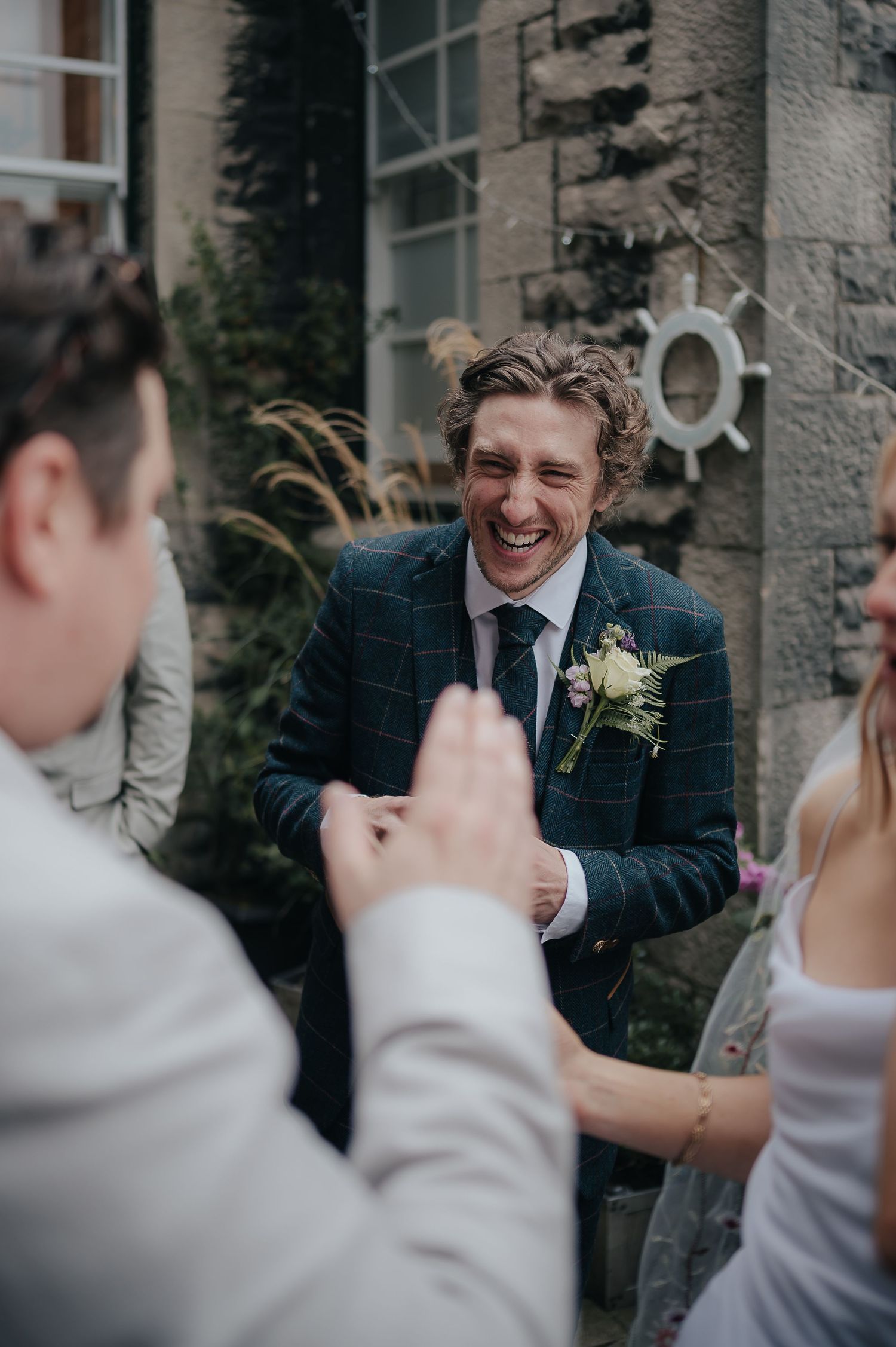 A candid moment of laughter during wedding celebrations outside a stone building.