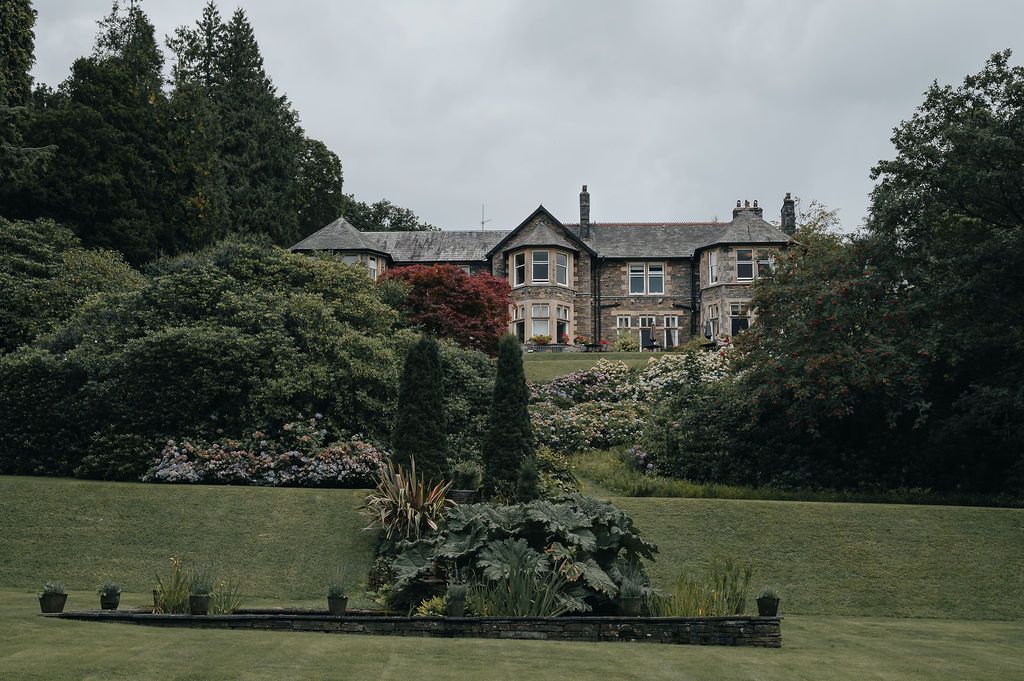 Elegant stone mansion set on a manicured lawn with evergreen trees and landscaping.