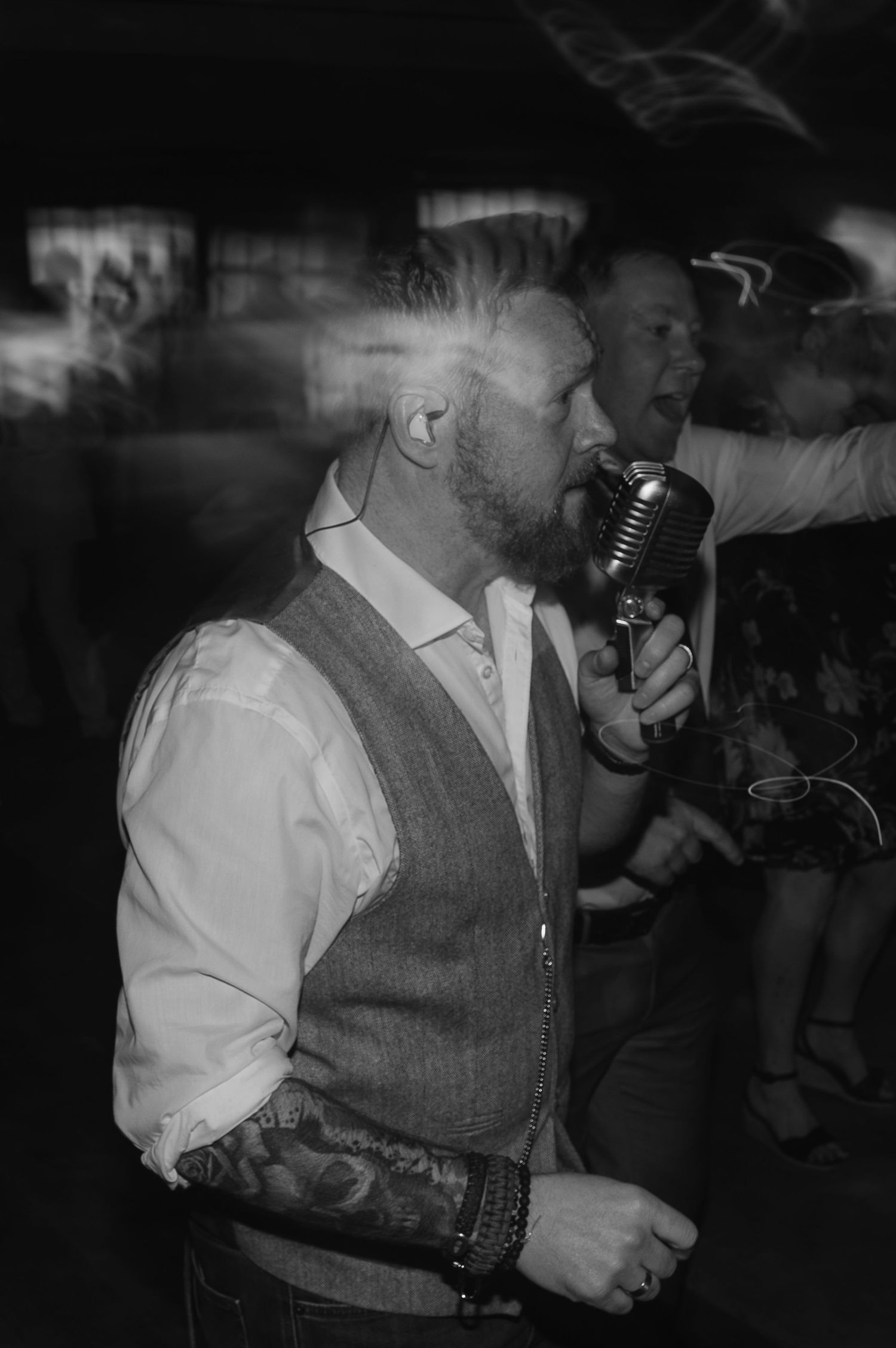 Person in a vest singing into vintage microphone at wedding reception.