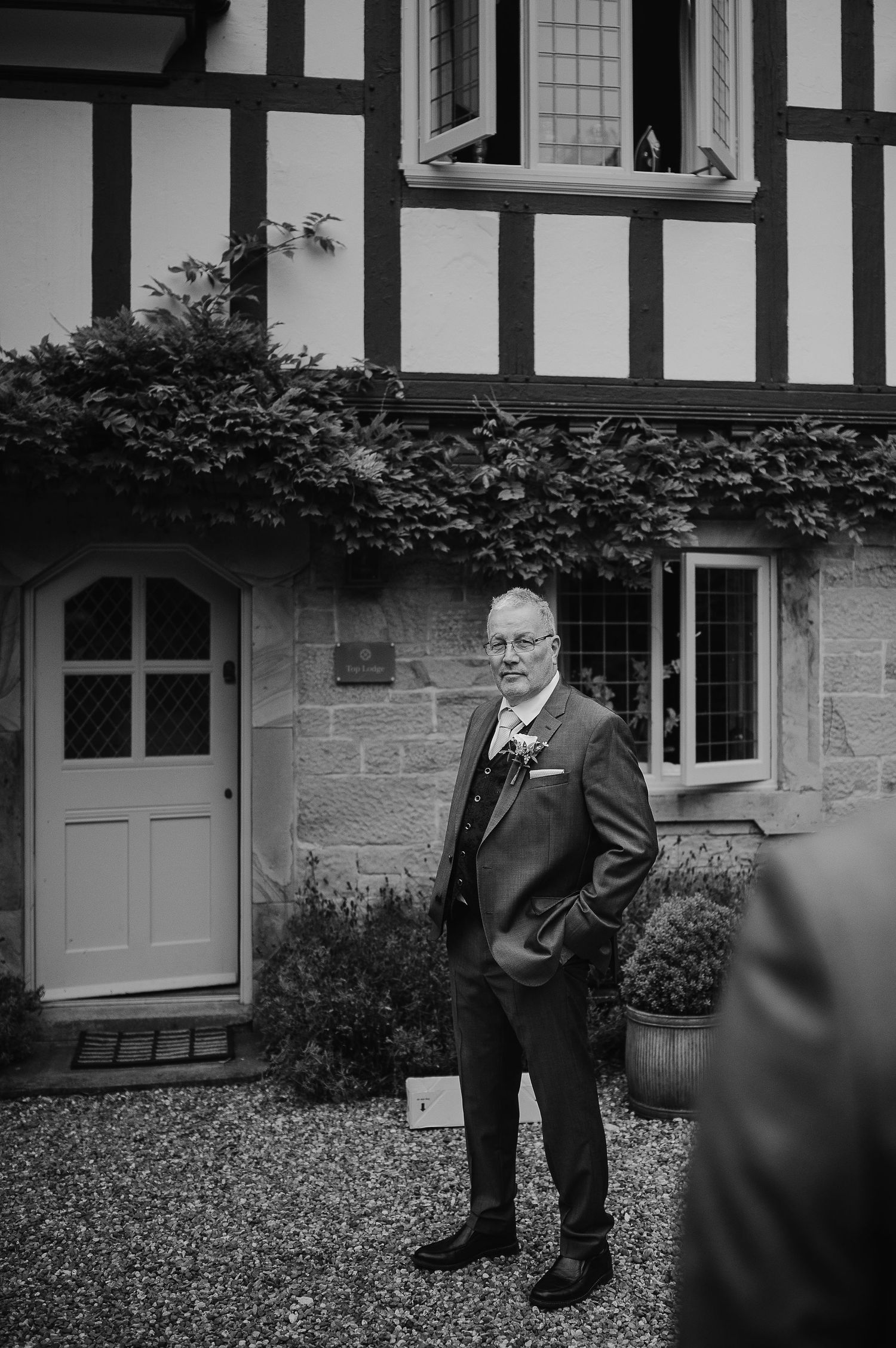 Black and white photo of a Tudor-style house exterior with ornate timber framing and stone base.