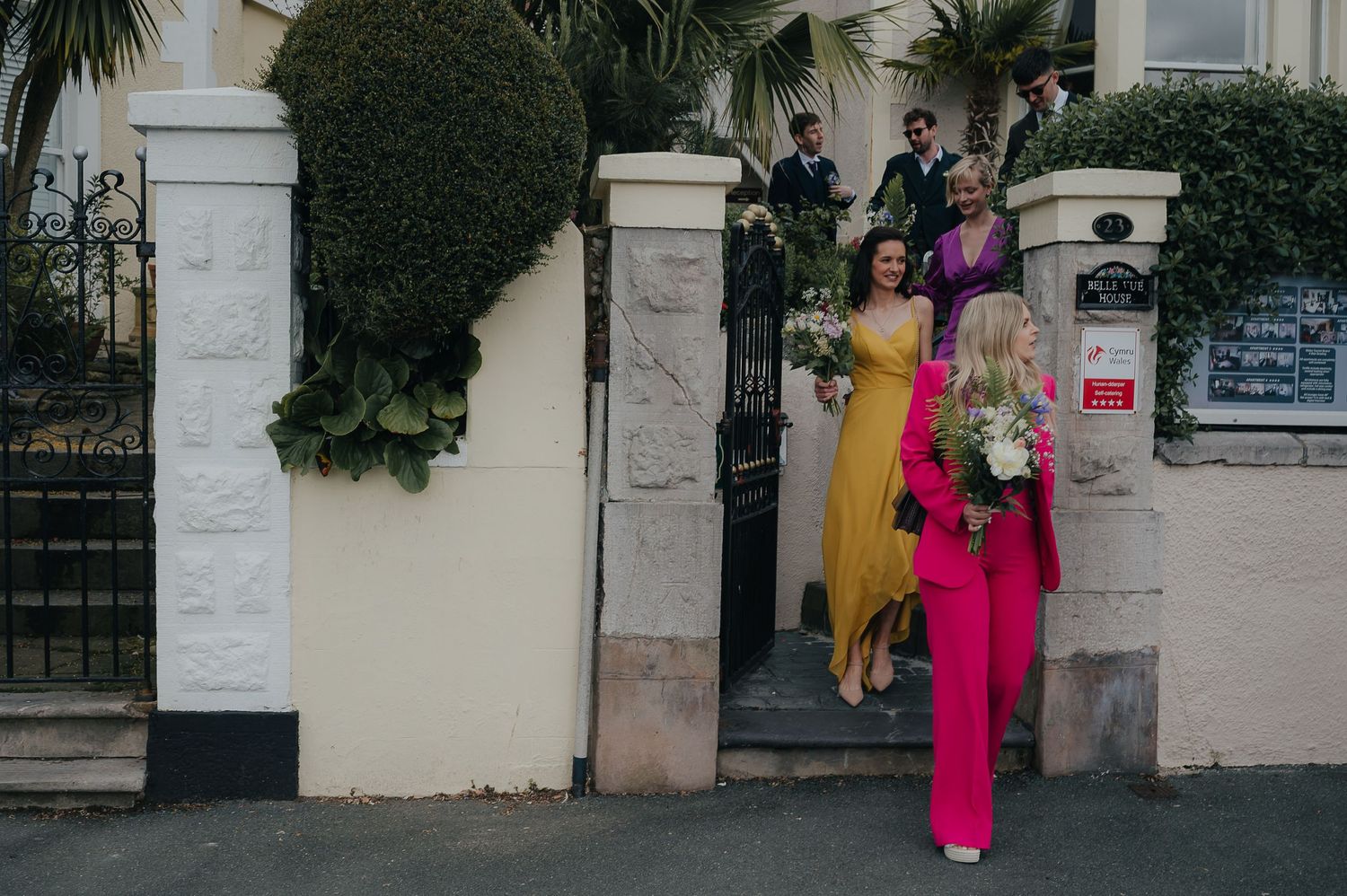 Two people in bright formal attire walking through an ornate stone gateway entrance.