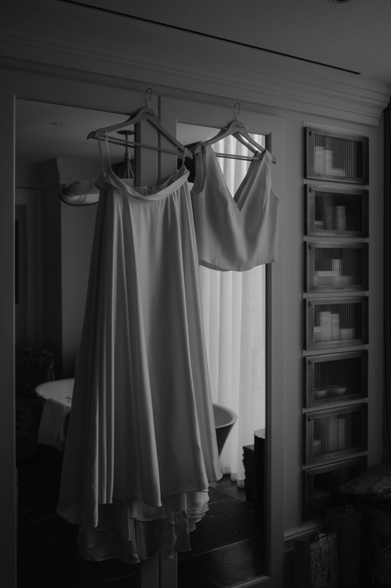 Wedding dress and formal attire hanging in a closet space beside built-in shelving units in black and white.