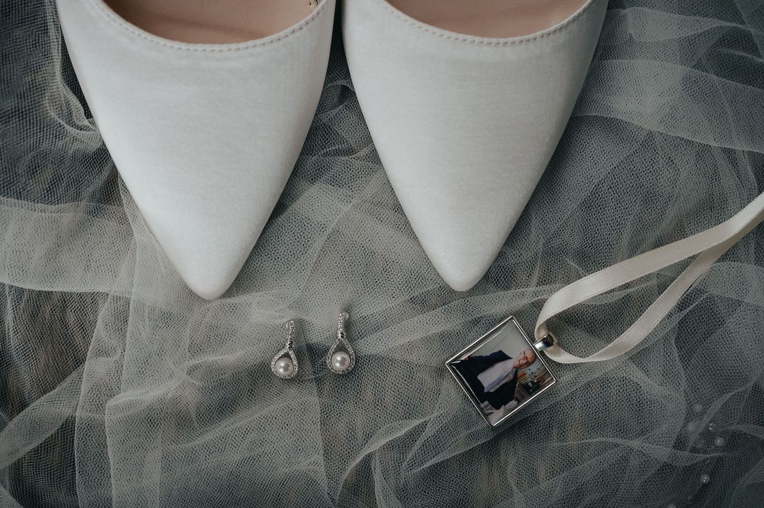 White bridal shoes, earrings and wedding accessories arranged on tulle fabric.