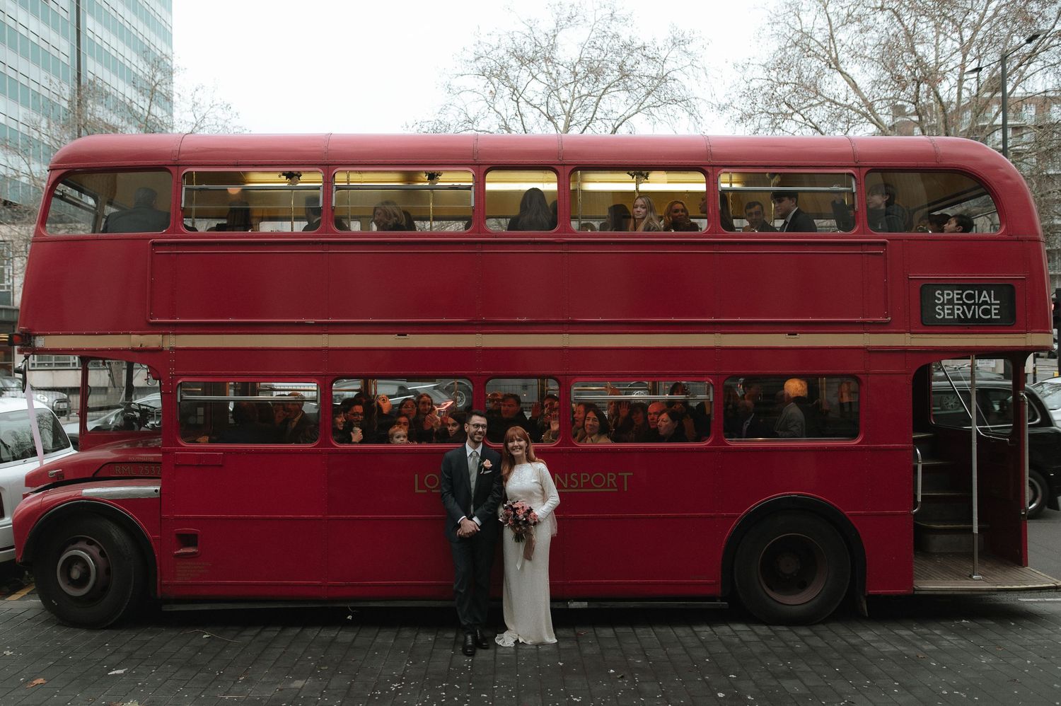 Bride and groom posing in front of a classic red London double-decker bus on their wedding day. London Wedding Photographer.
