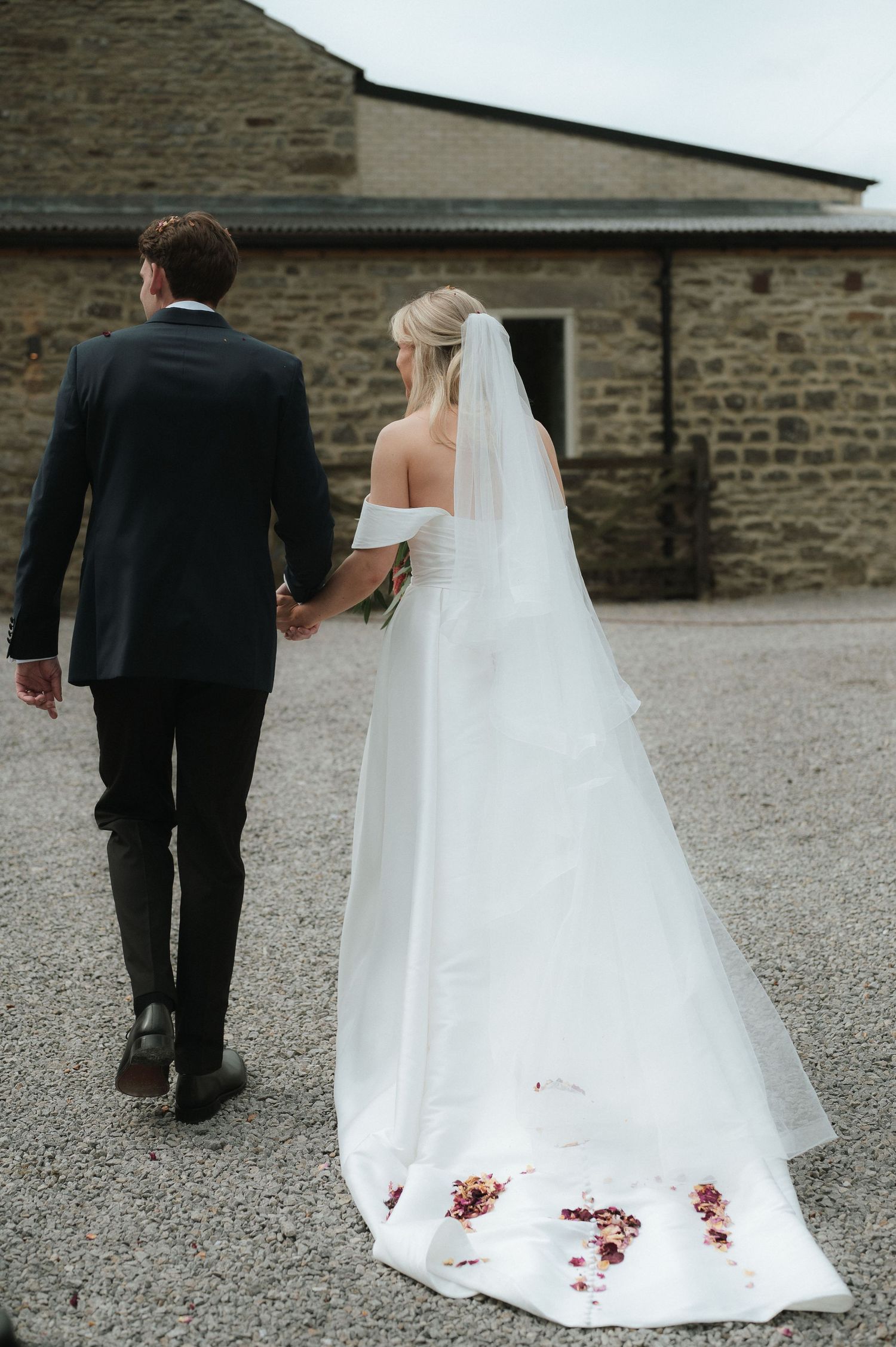 A wedding couple walking away from camera showing the long train of the bride's white dress.