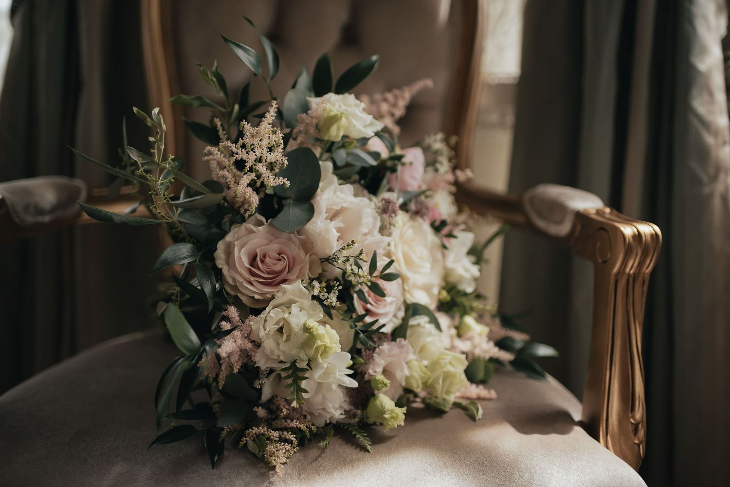 Elegant wedding bouquet with pink and white roses and mixed greenery resting on an antique chair.