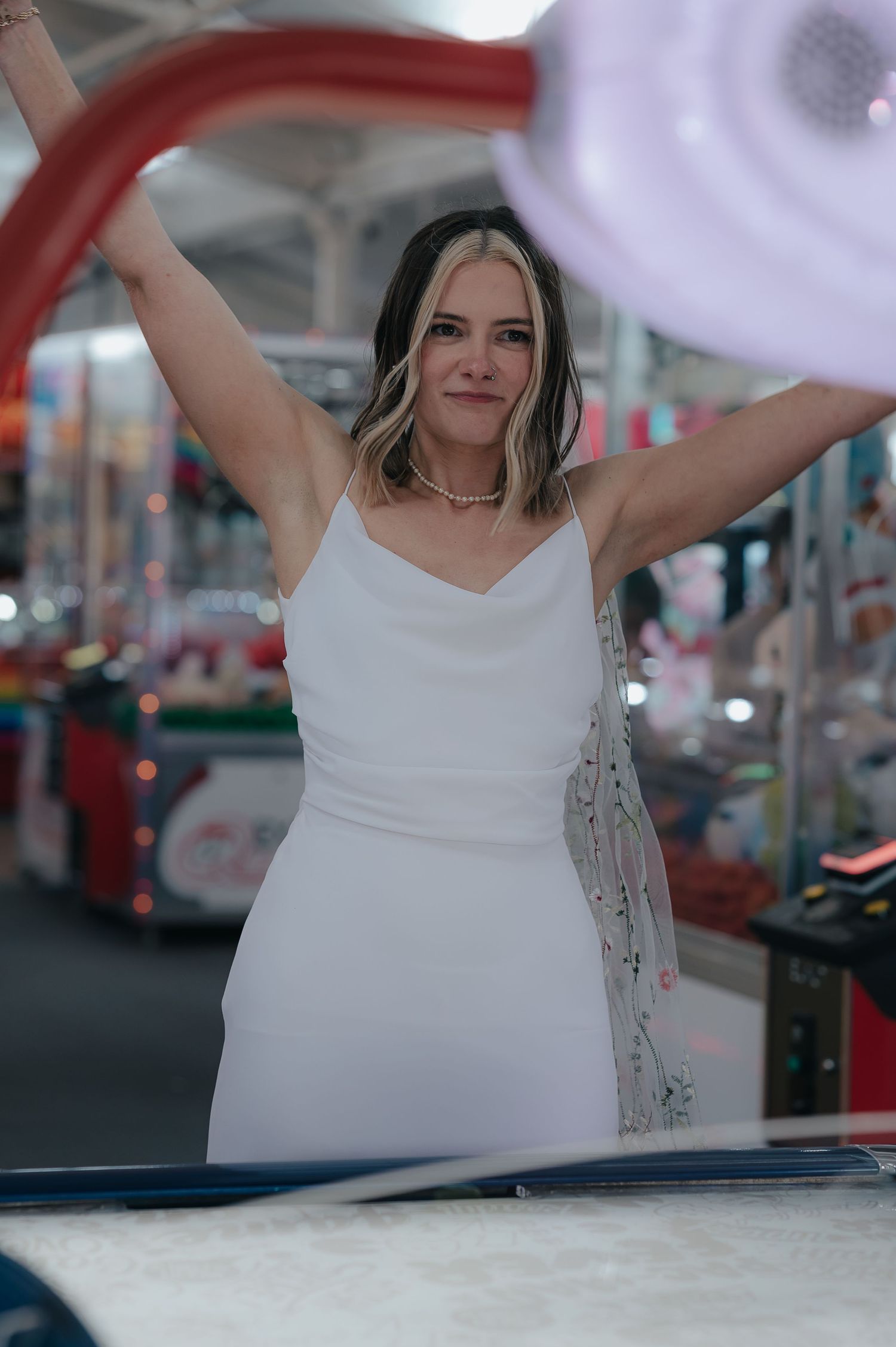 Bride in simple white dress celebrating at an arcade venue.