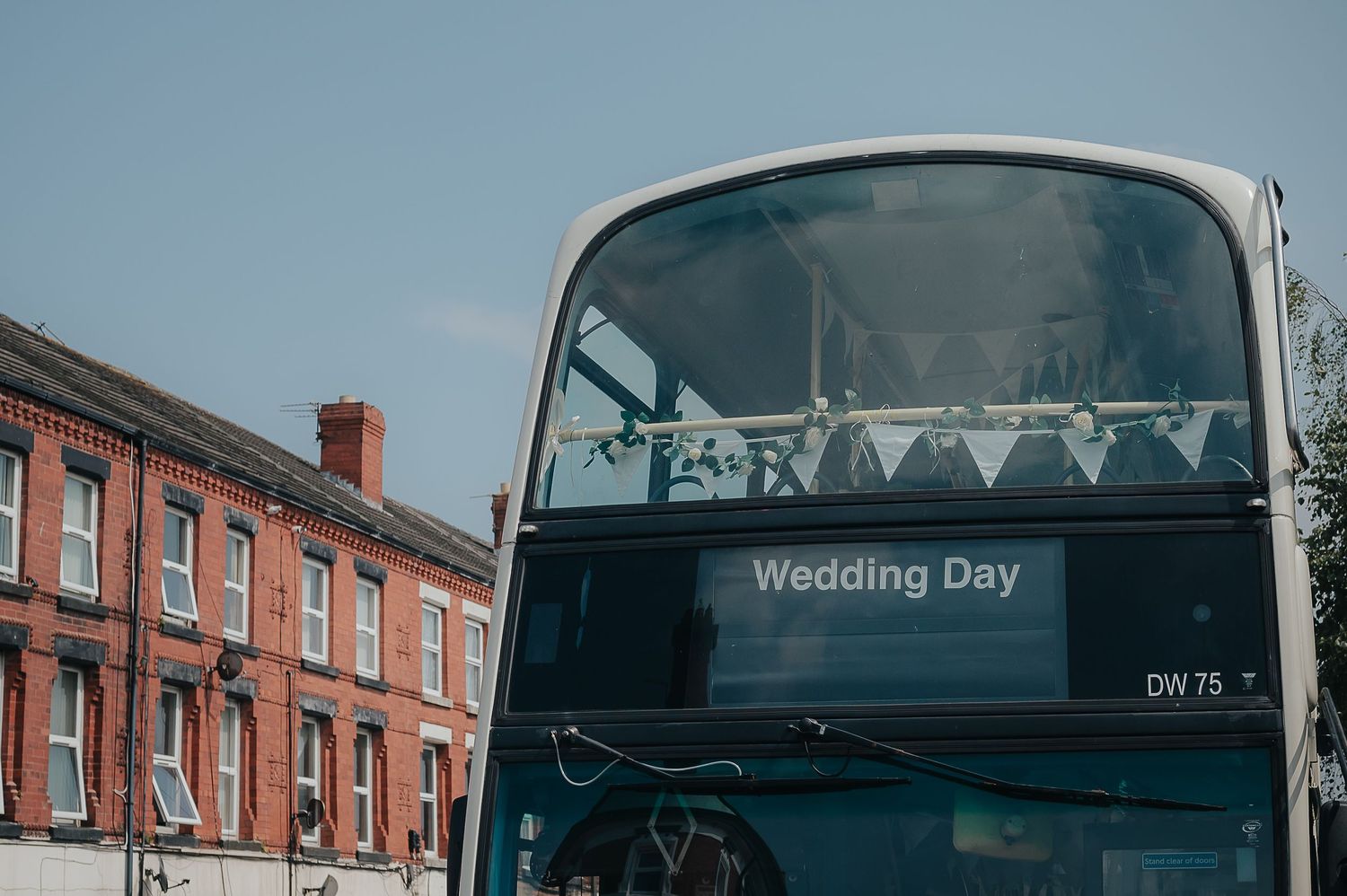 A double-decker bus with 'Wedding Day' displayed on its destination board against a blue sky.