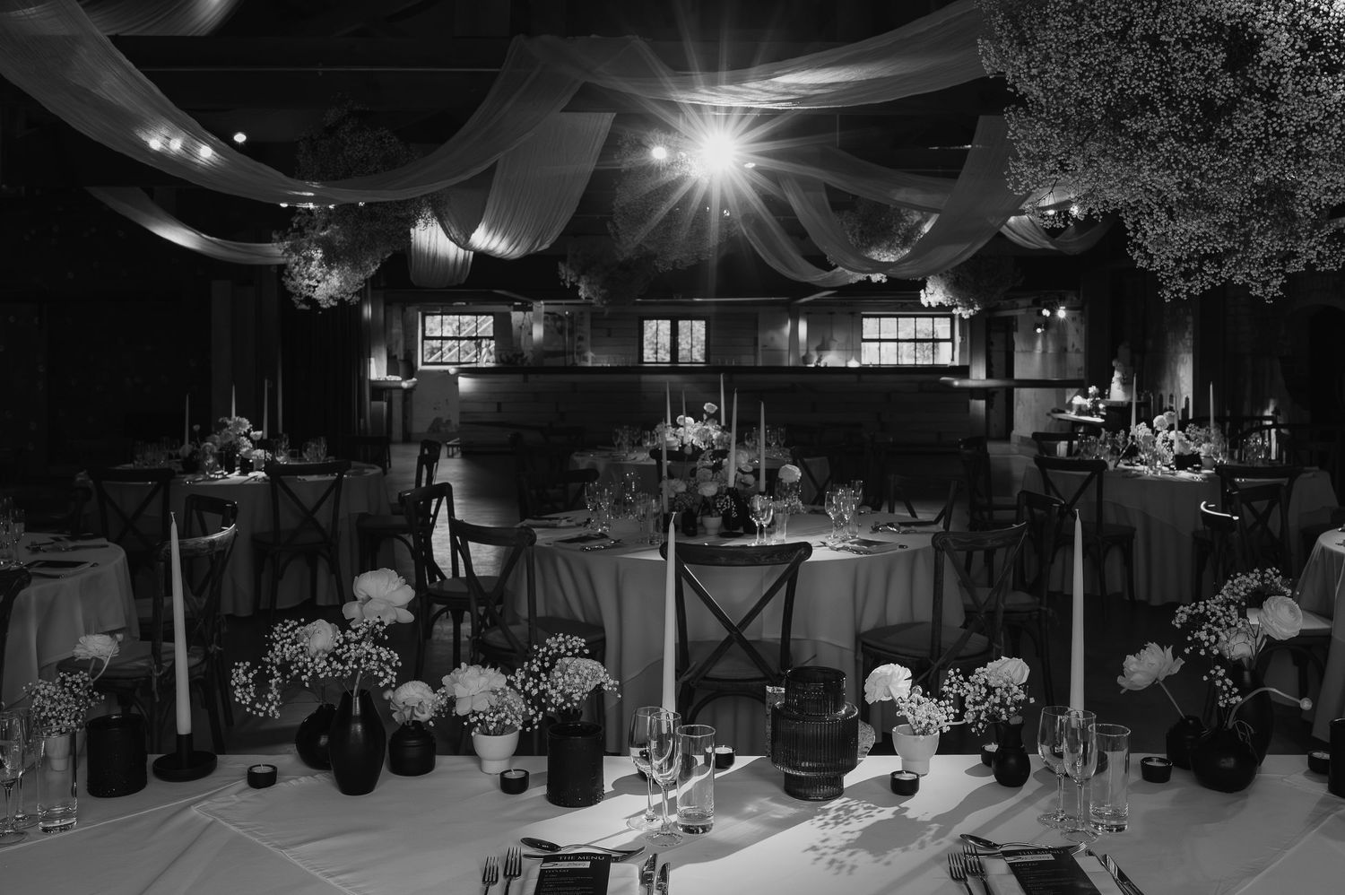 Black and white photo of an elegant wedding reception venue with floral centerpieces.