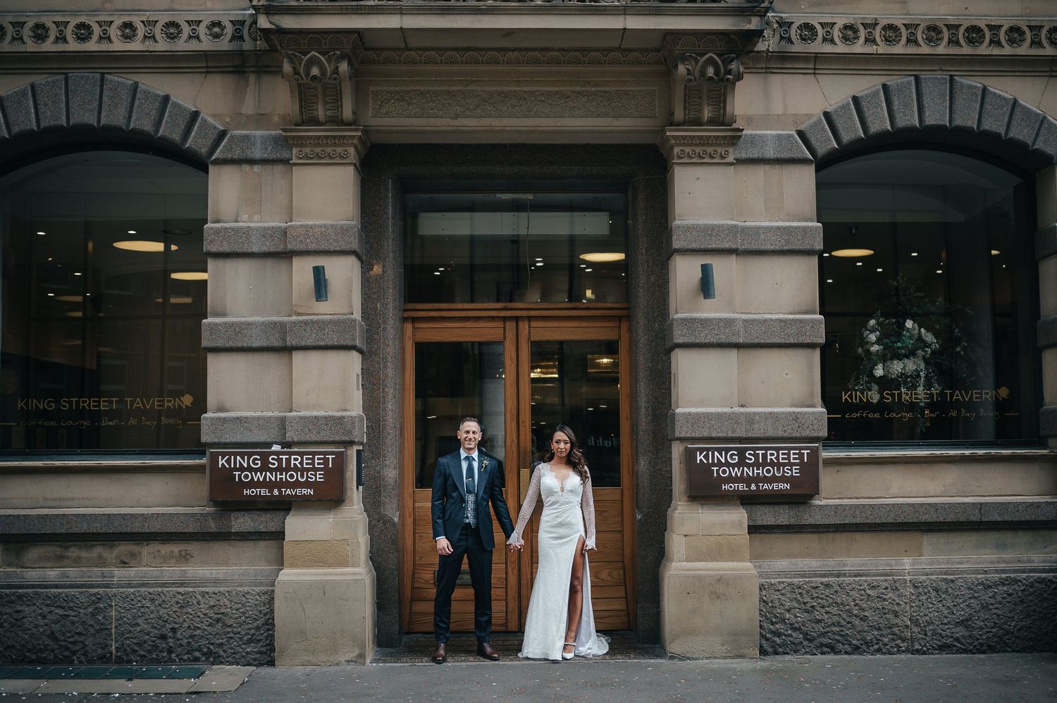 Couple stands in doorway of historic stone building on wedding day.