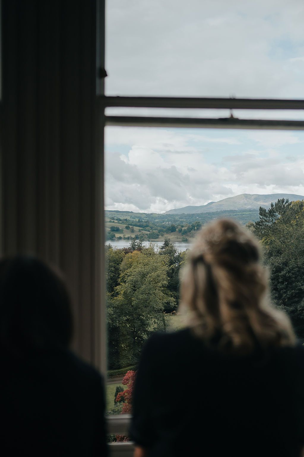 Two silhouettes looking out window at scenic mountain landscape view.