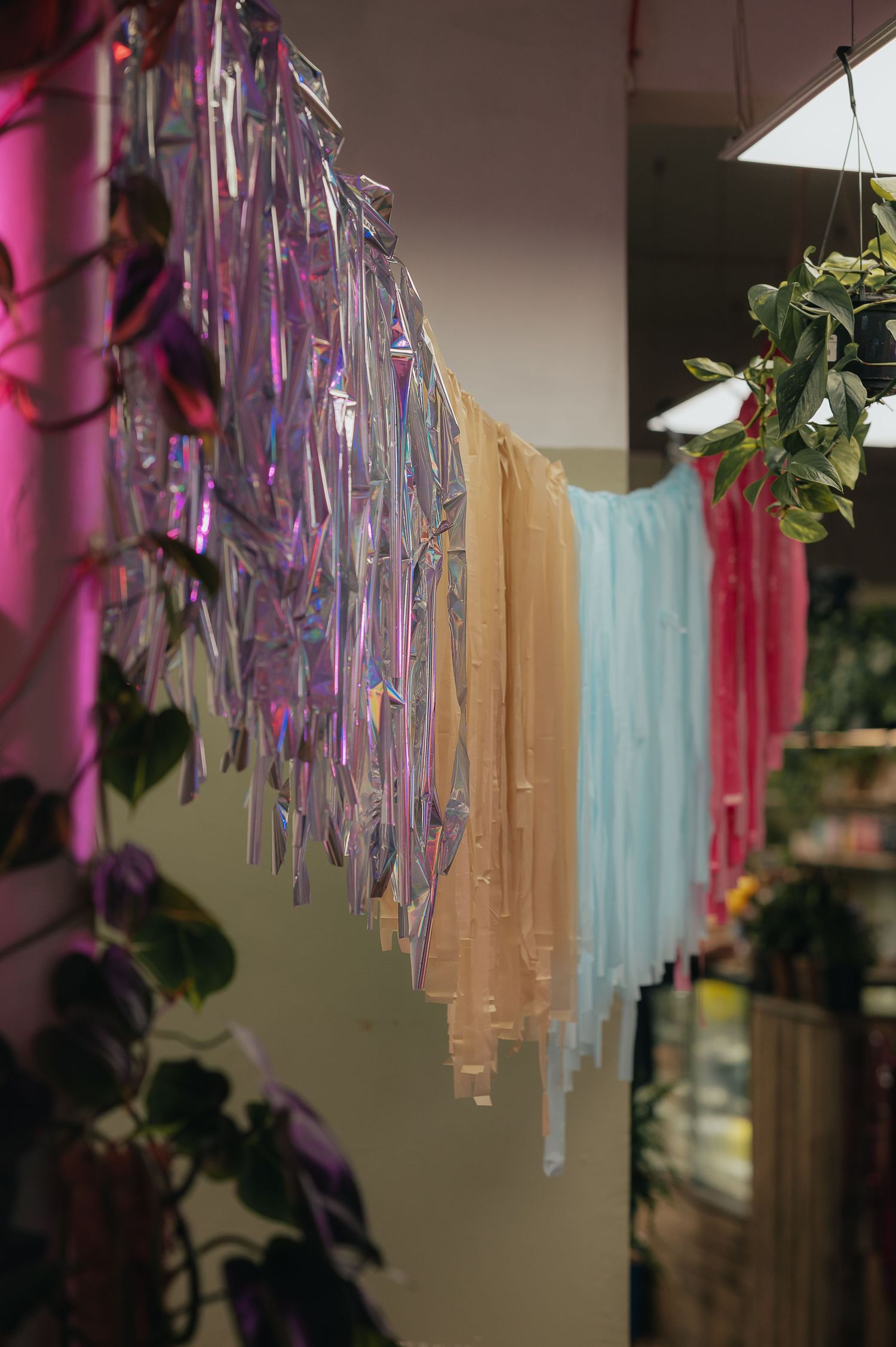 Colorful iridescent and pastel streamers hanging from ceiling with greenery decorations.