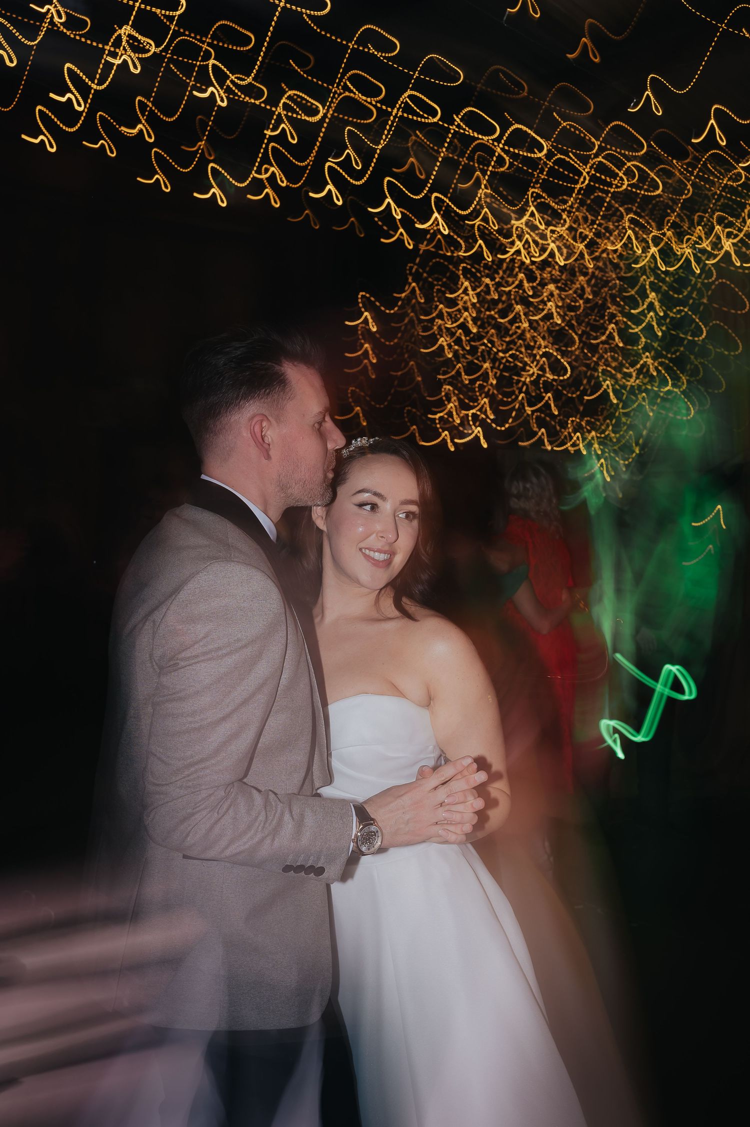 Couple sharing an intimate dance moment under golden string lights at wedding reception.