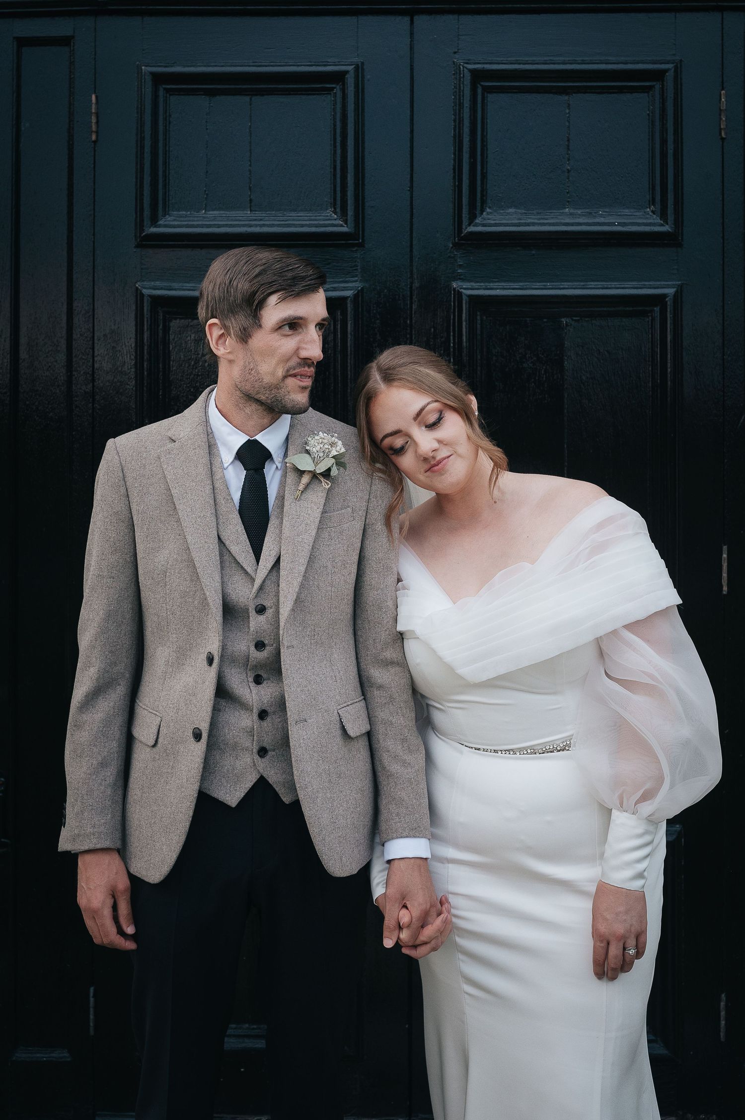 Elegant wedding portrait against dark door featuring classic formal attire.