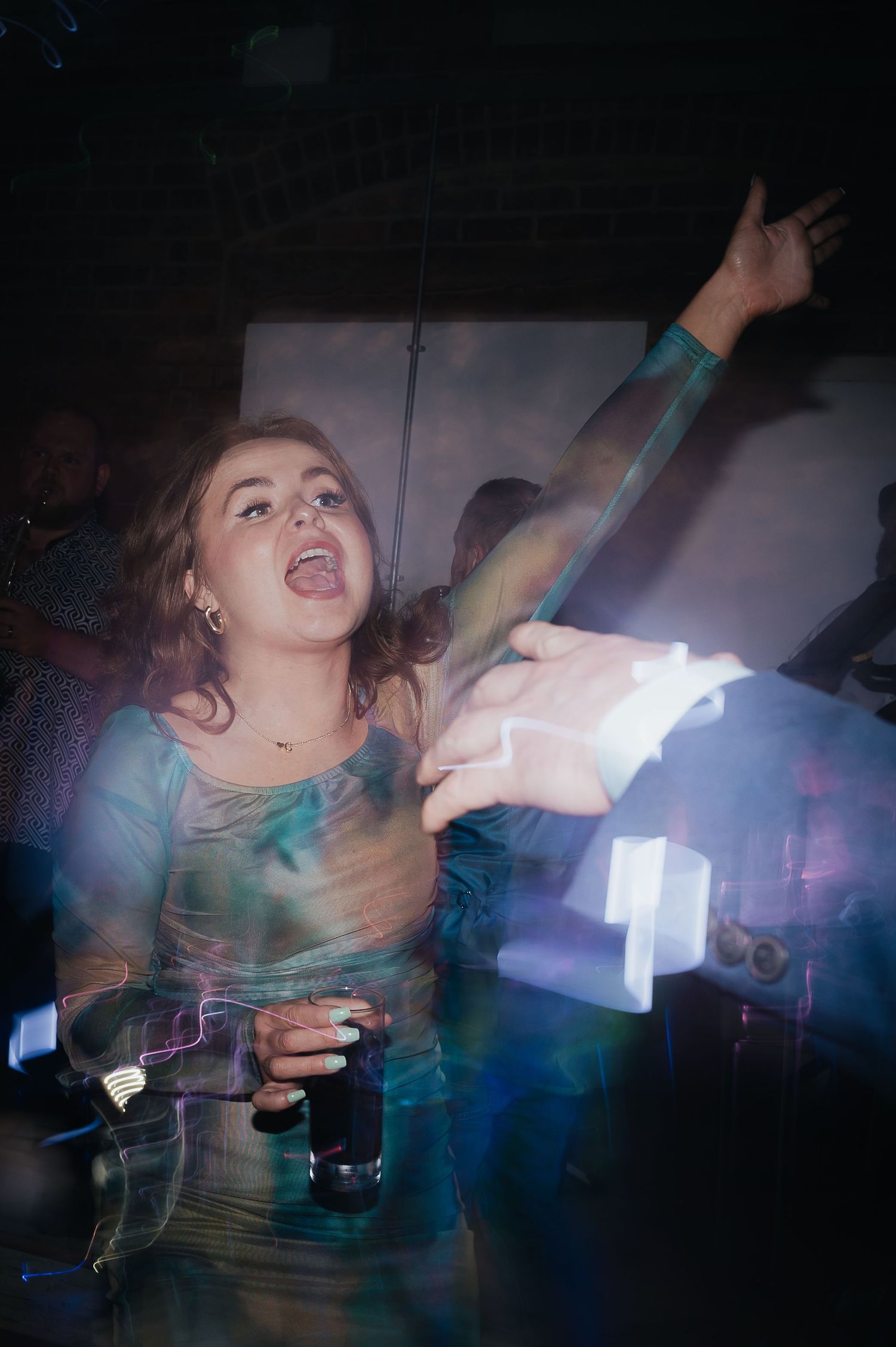 Party guest dancing energetically with raised arms holding a drink in a dark nightclub setting.