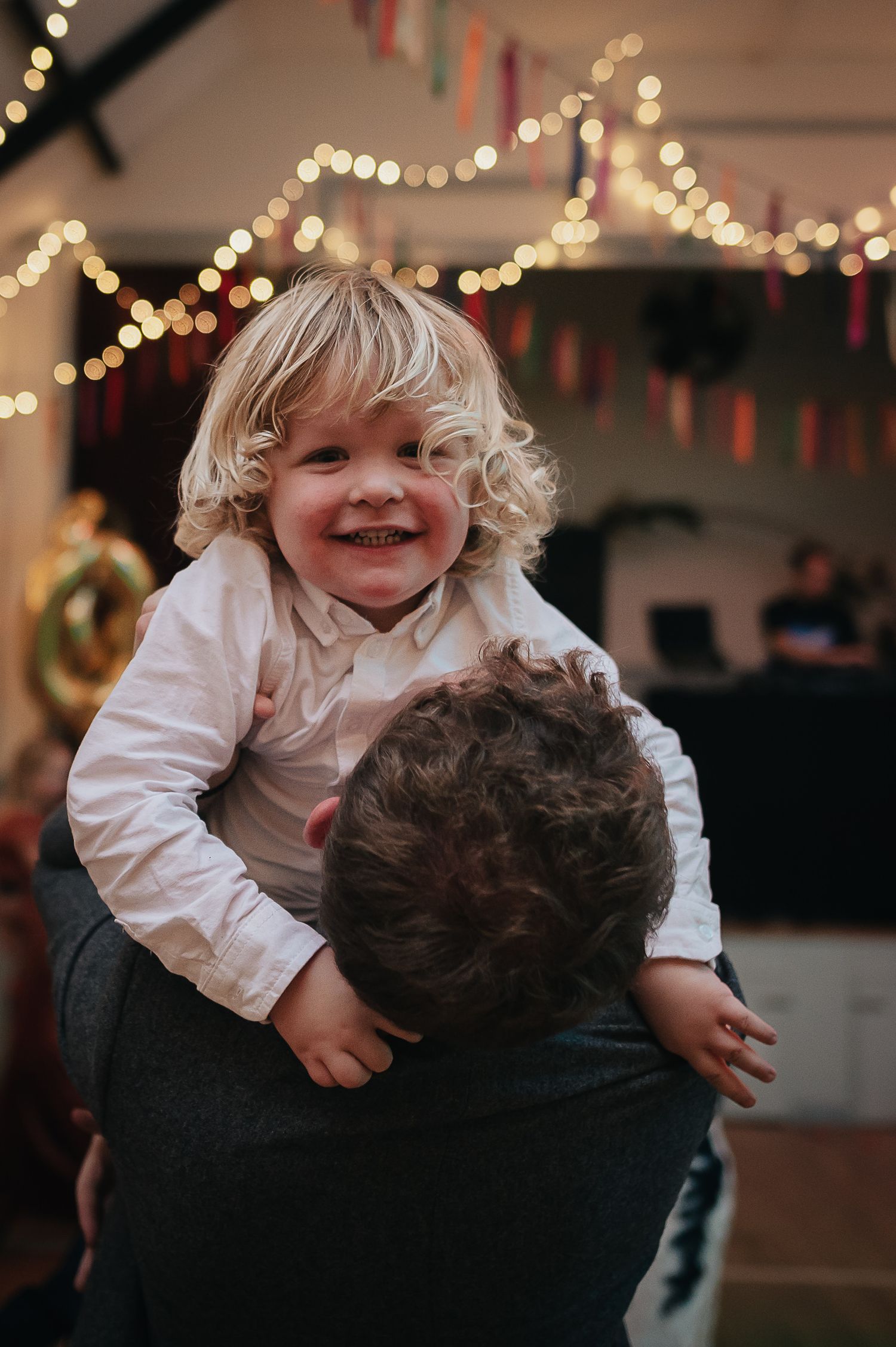 Joyful dancing moment at wedding reception with string lights and festive decorations overhead.