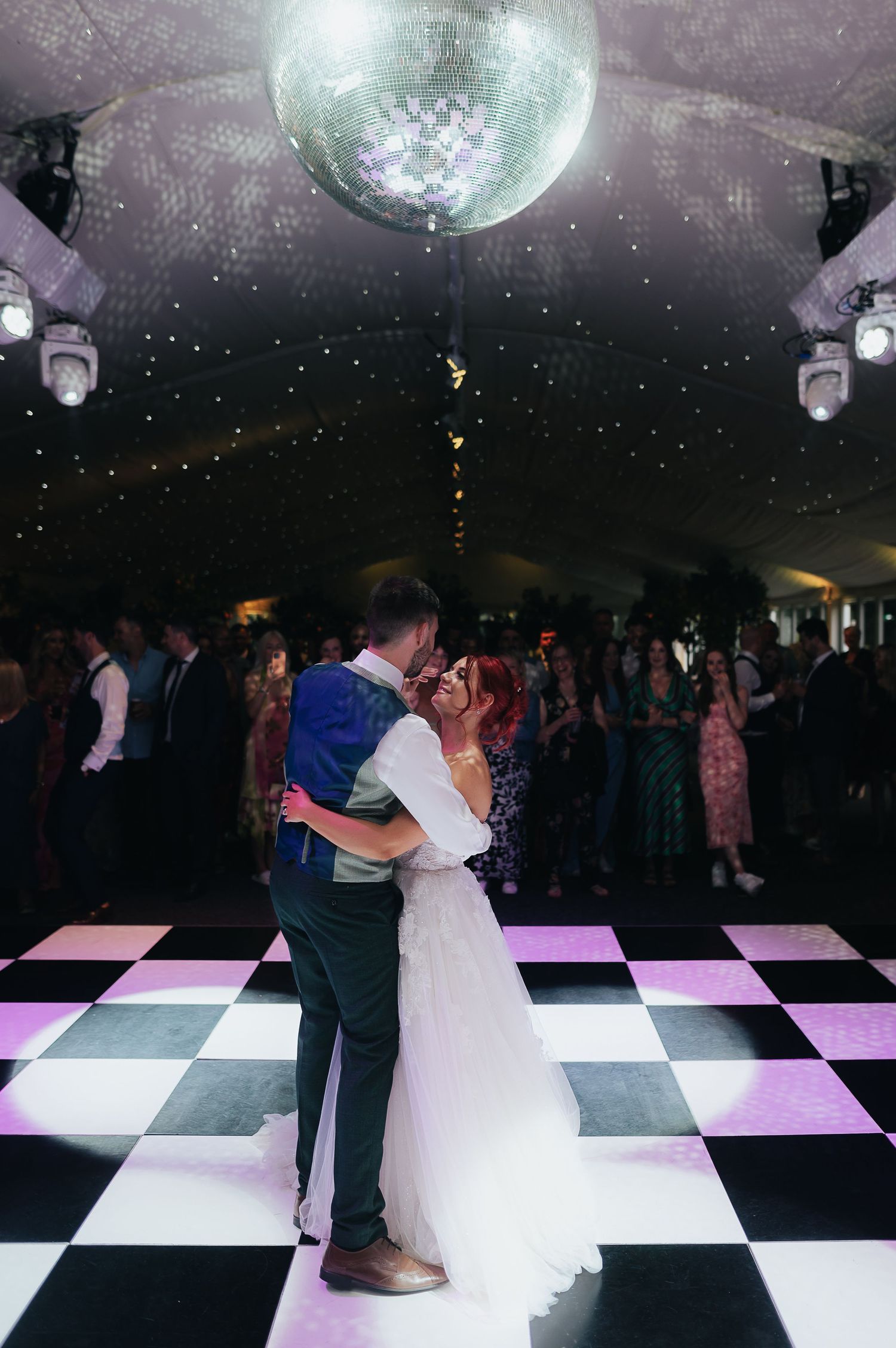 Couple dancing under a disco ball on a black and white checkered dance floor.
