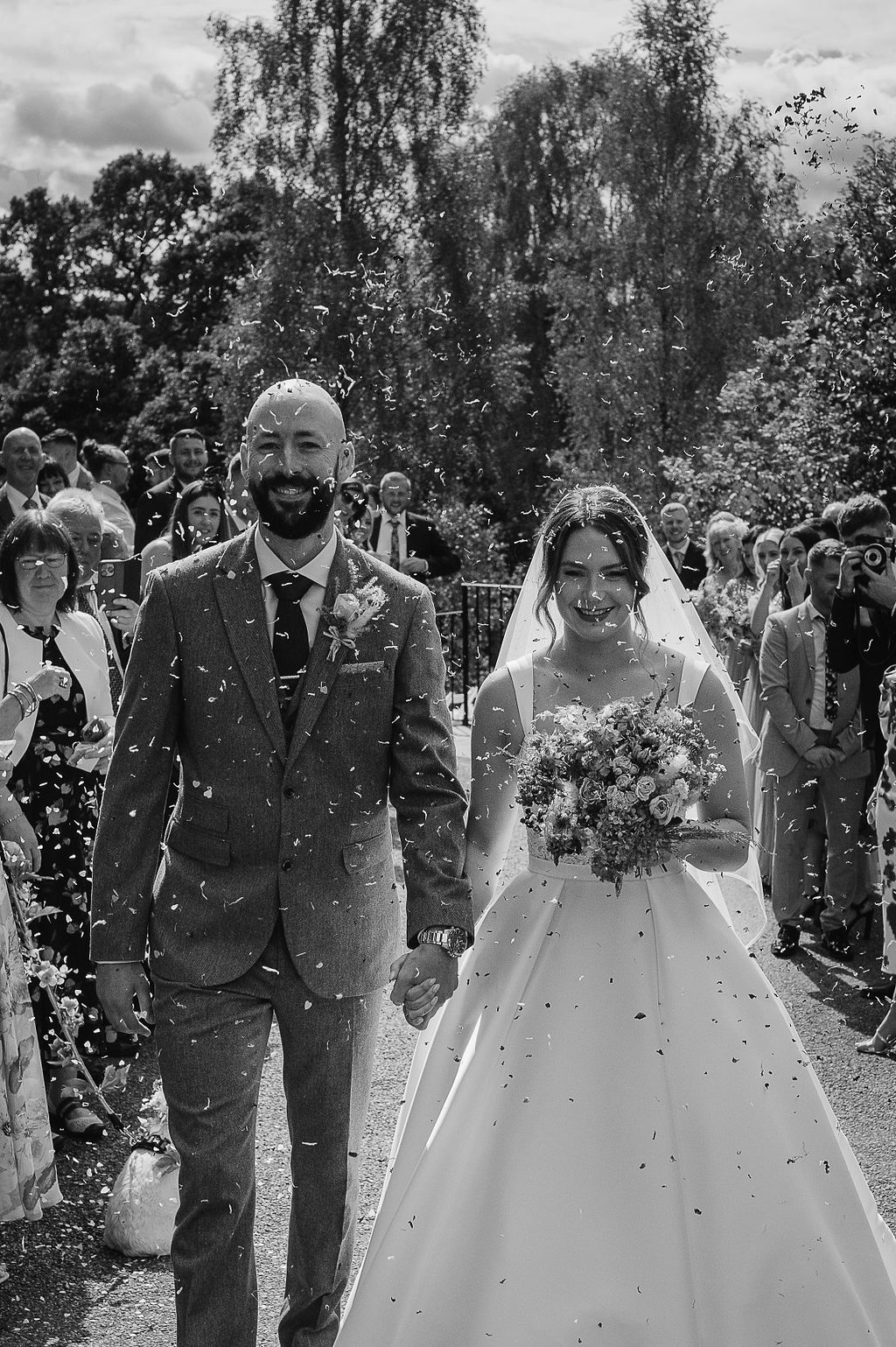 Newlyweds walking down path while guests throw confetti in celebration.