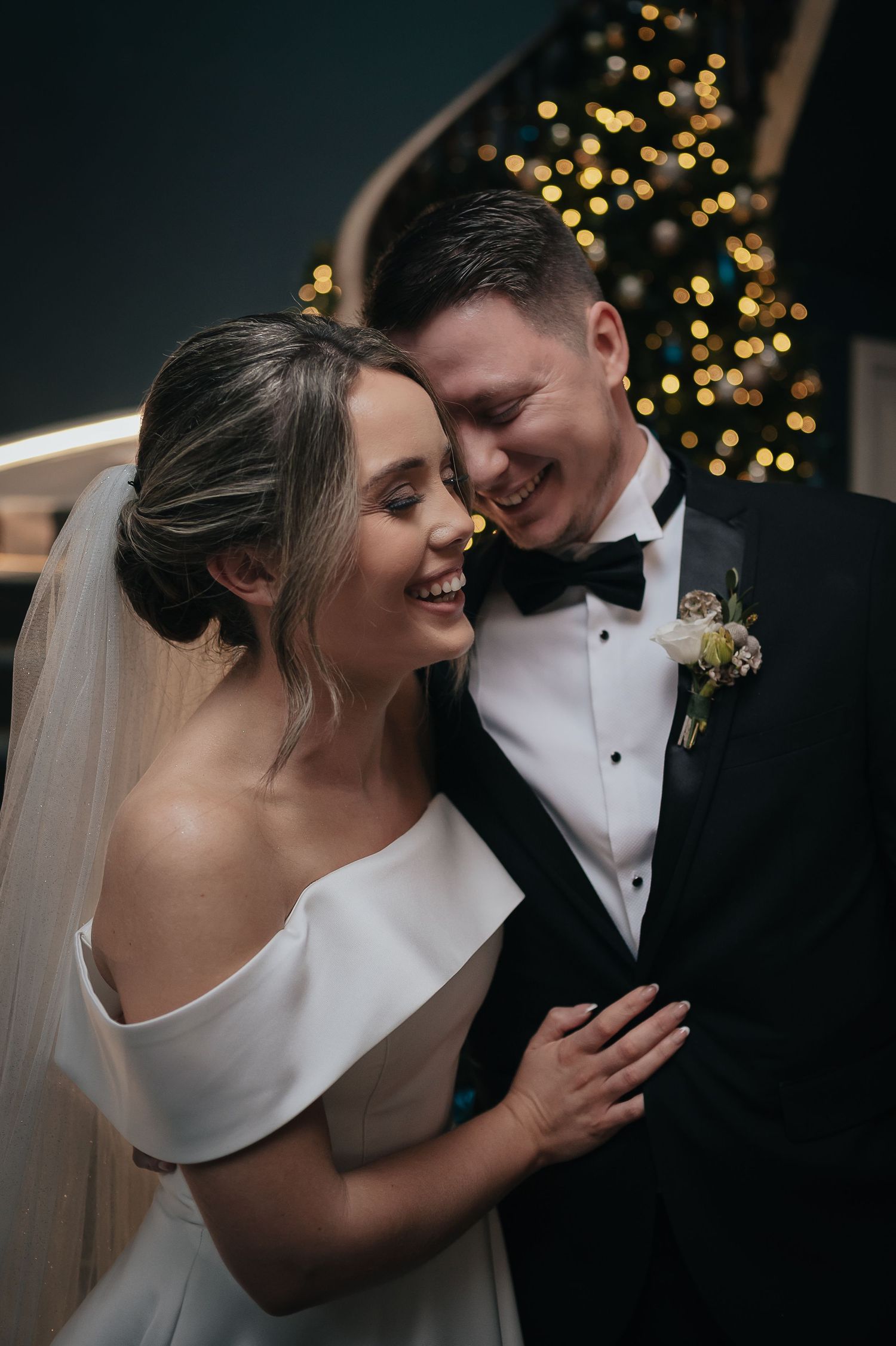 Intimate wedding portrait of newlyweds sharing a joyful moment with twinkling lights in the background.
