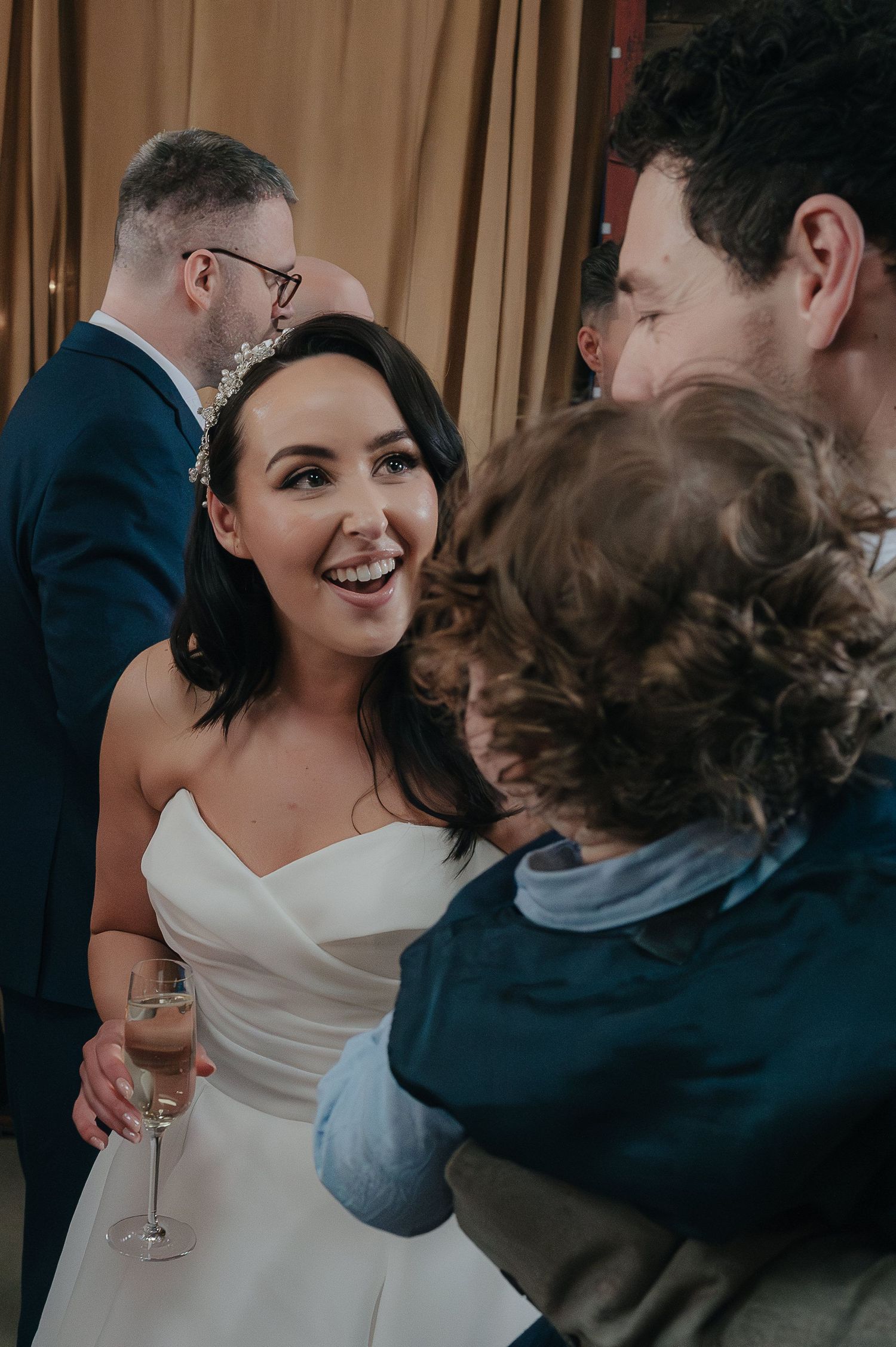 Wedding celebration with guests enjoying champagne and conversations at an indoor reception.