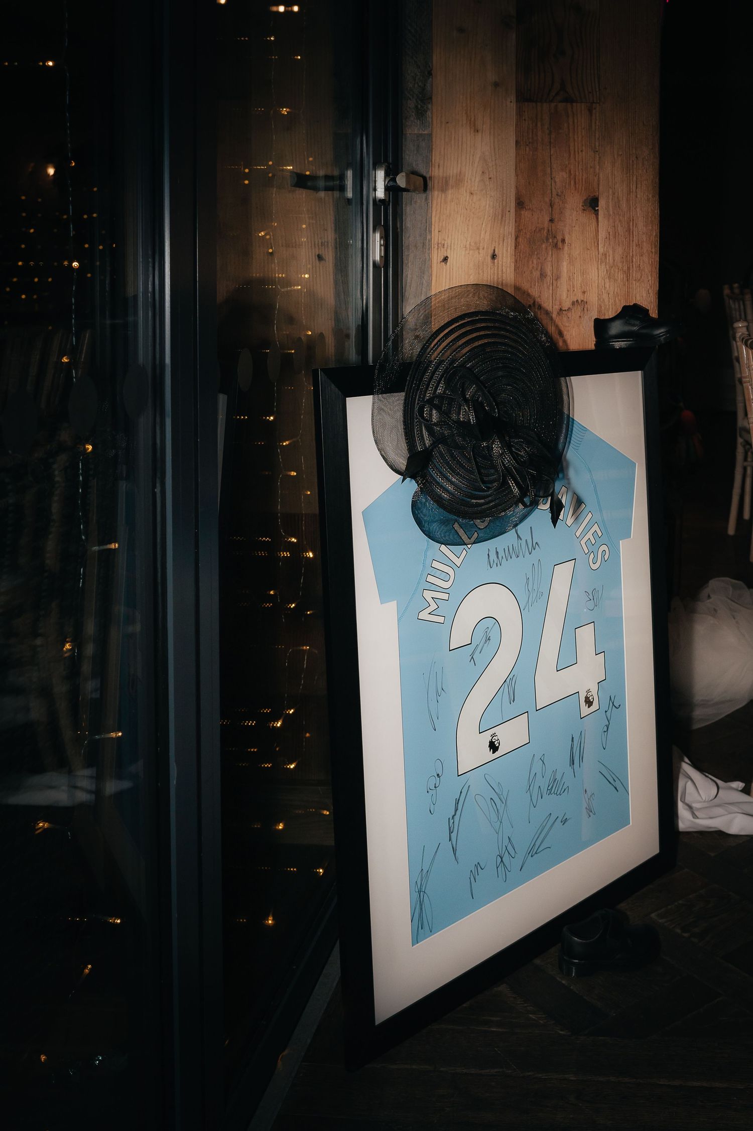 A framed light blue sports jersey with number 24 sits against a dark wall with twinkling lights in the background.