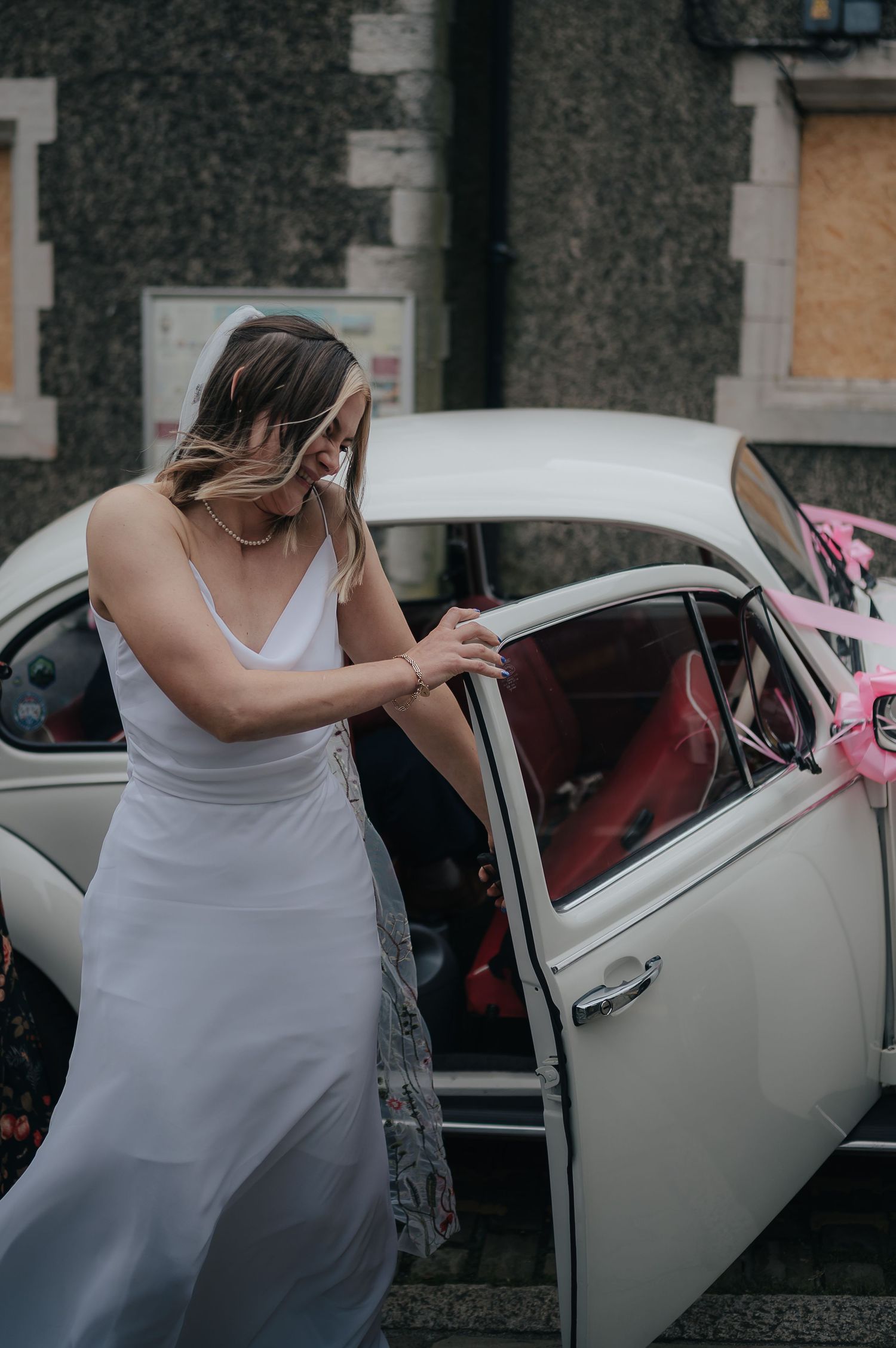 A white wedding dress and classic car create an elegant entrance scene on a moody day.