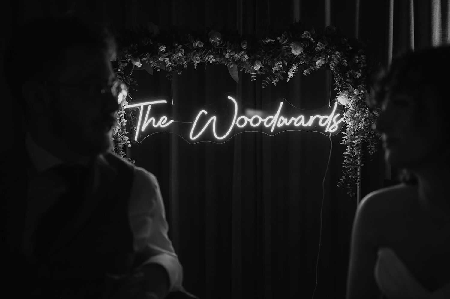 An illuminated neon sign reading 'The Woodwards' with floral arch decoration.