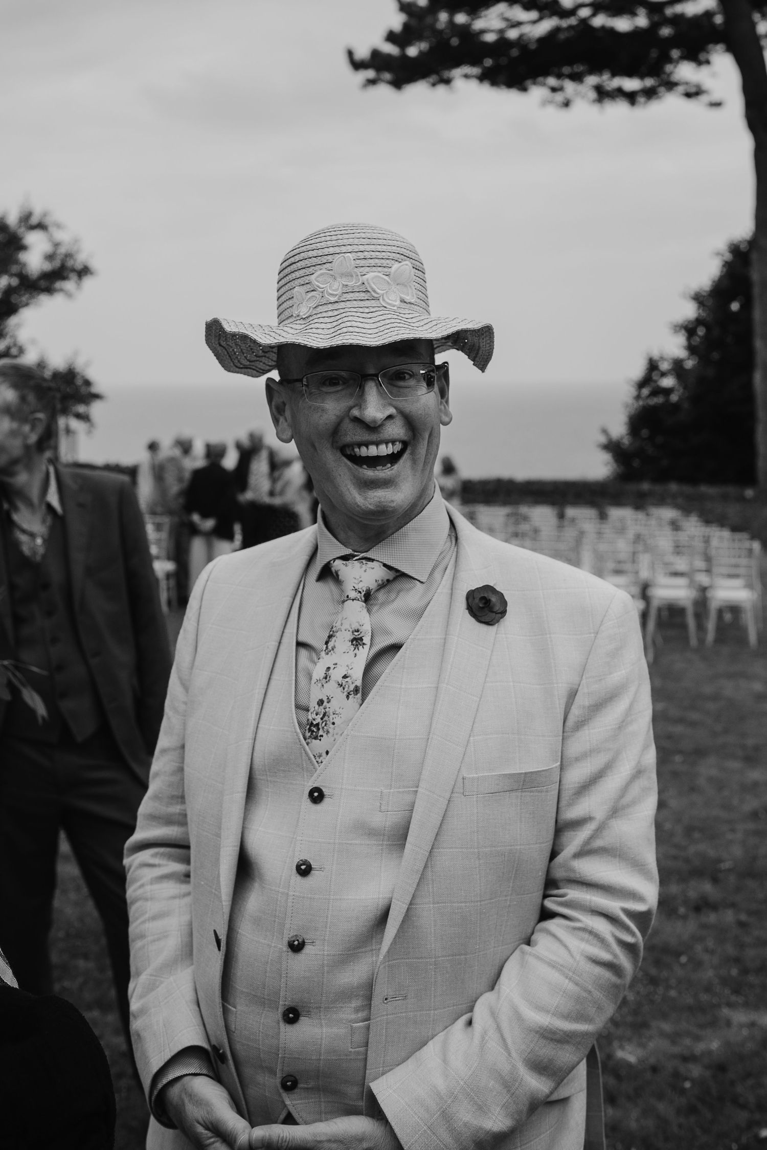 Guest at outdoor wedding wearing light colored suit and striped sun hat.