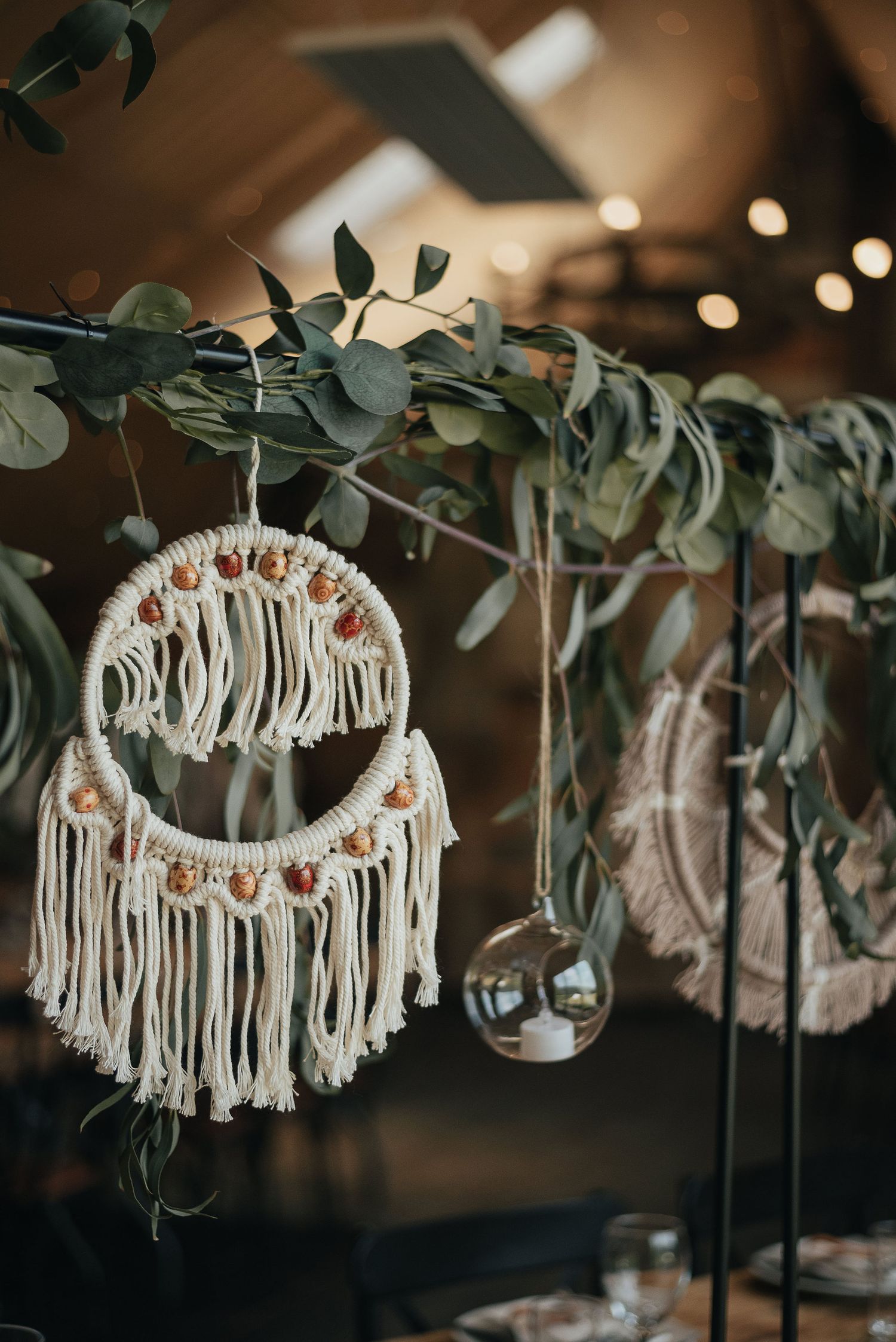 Macrame dream catcher with eucalyptus leaves and string lights creating bohemian wedding decor.