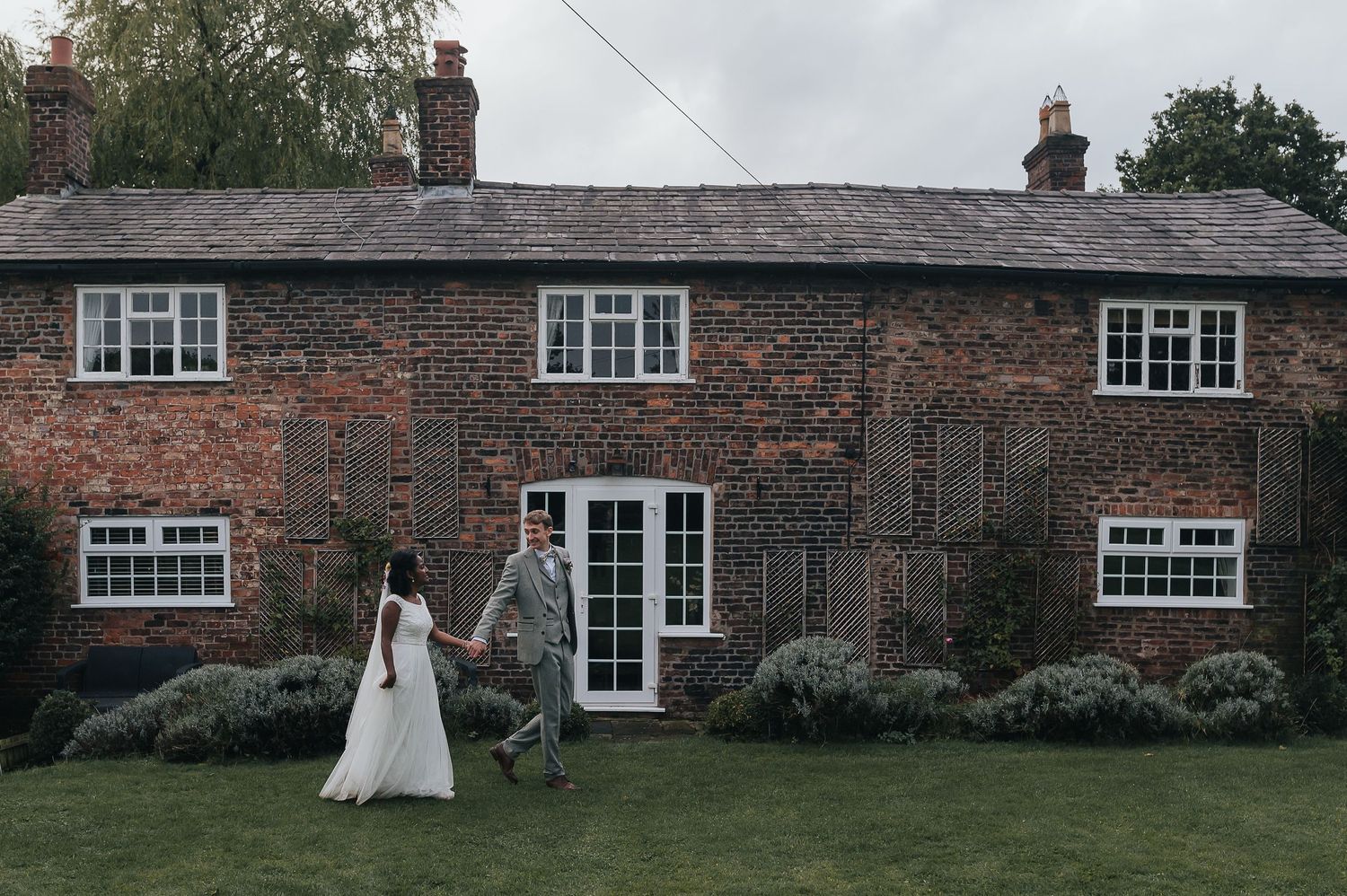 Newlyweds walking outside traditional brick cottage with garden landscaping.