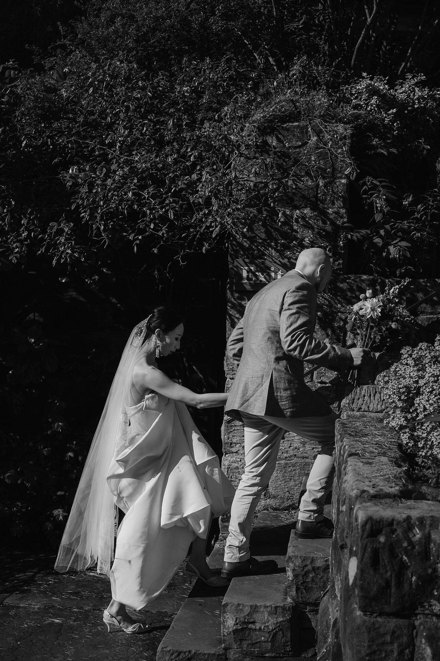A black and white photo captures movement on stone steps surrounded by foliage.