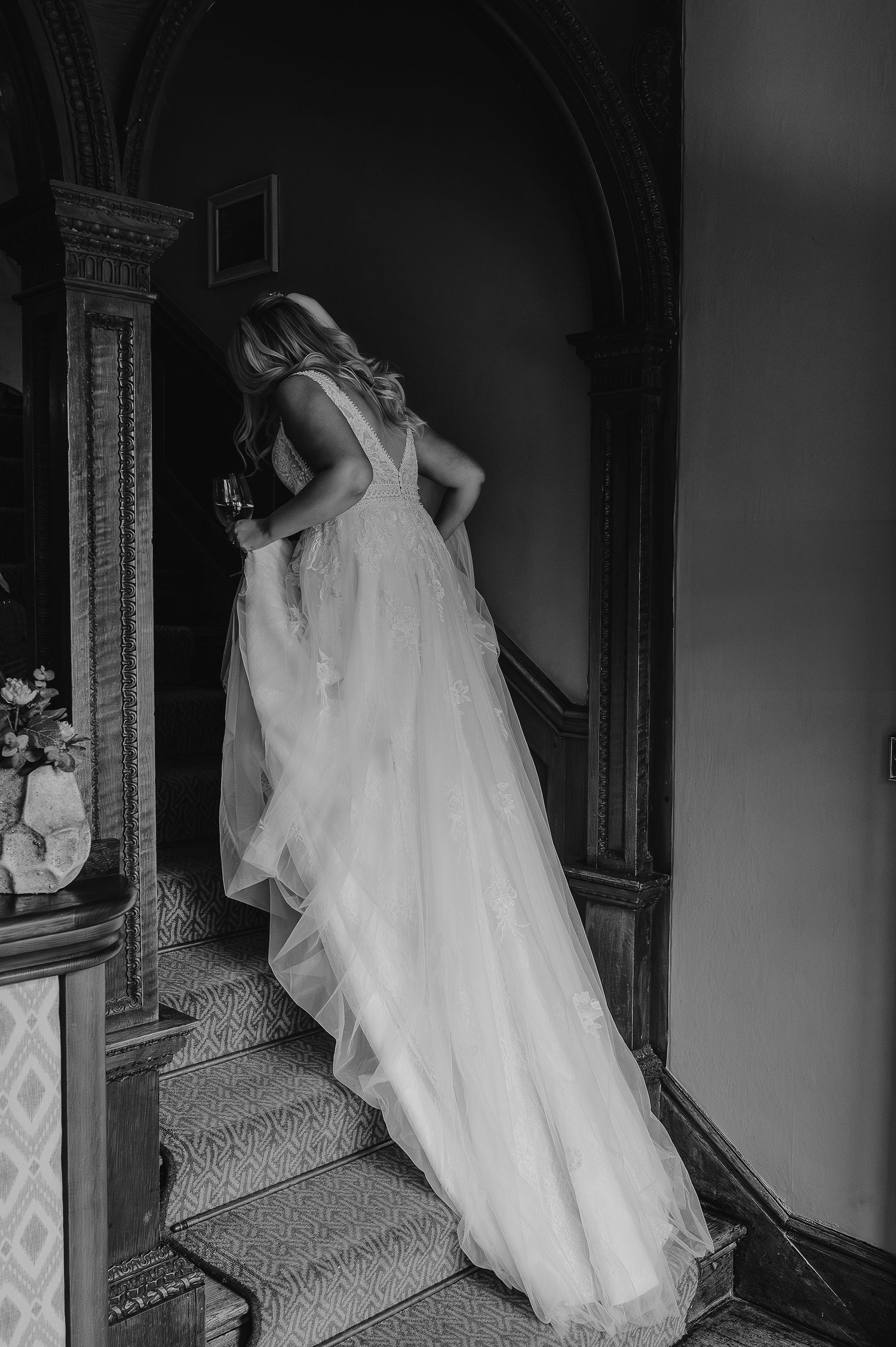 Flowing white wedding dress cascades down ornate staircase in dramatic black and white photography.